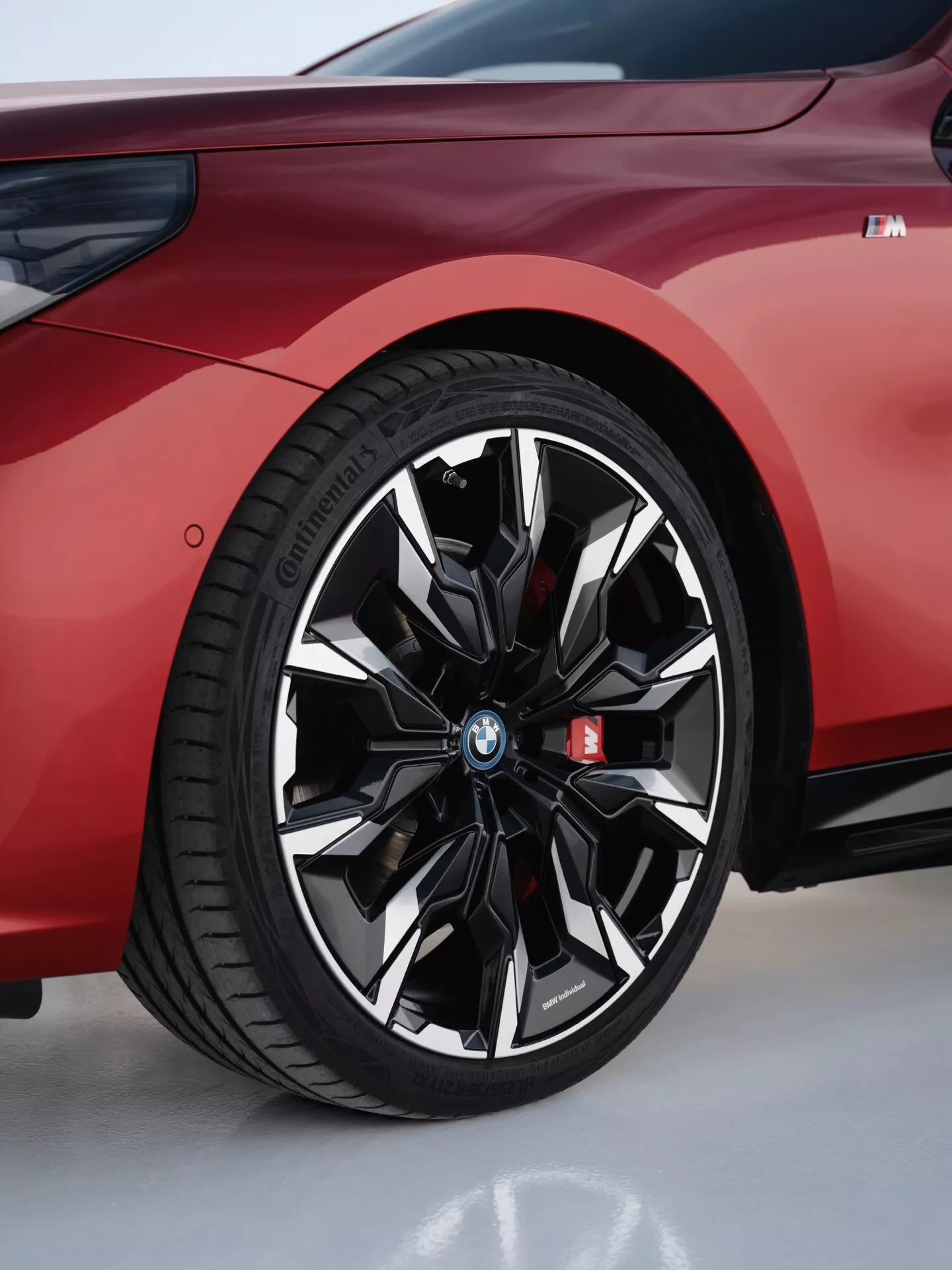 Podroben pogled na sprednje kolo BMW serije 5 2023 (G60-G61) z dinamičnim dizajnom multi-kraka v sijajno črni in kovinskih finiših z Continental pnevmatiko, poudarjen z logotipom BMW in 'M' emblemo, pred živo rdečim ohišjem