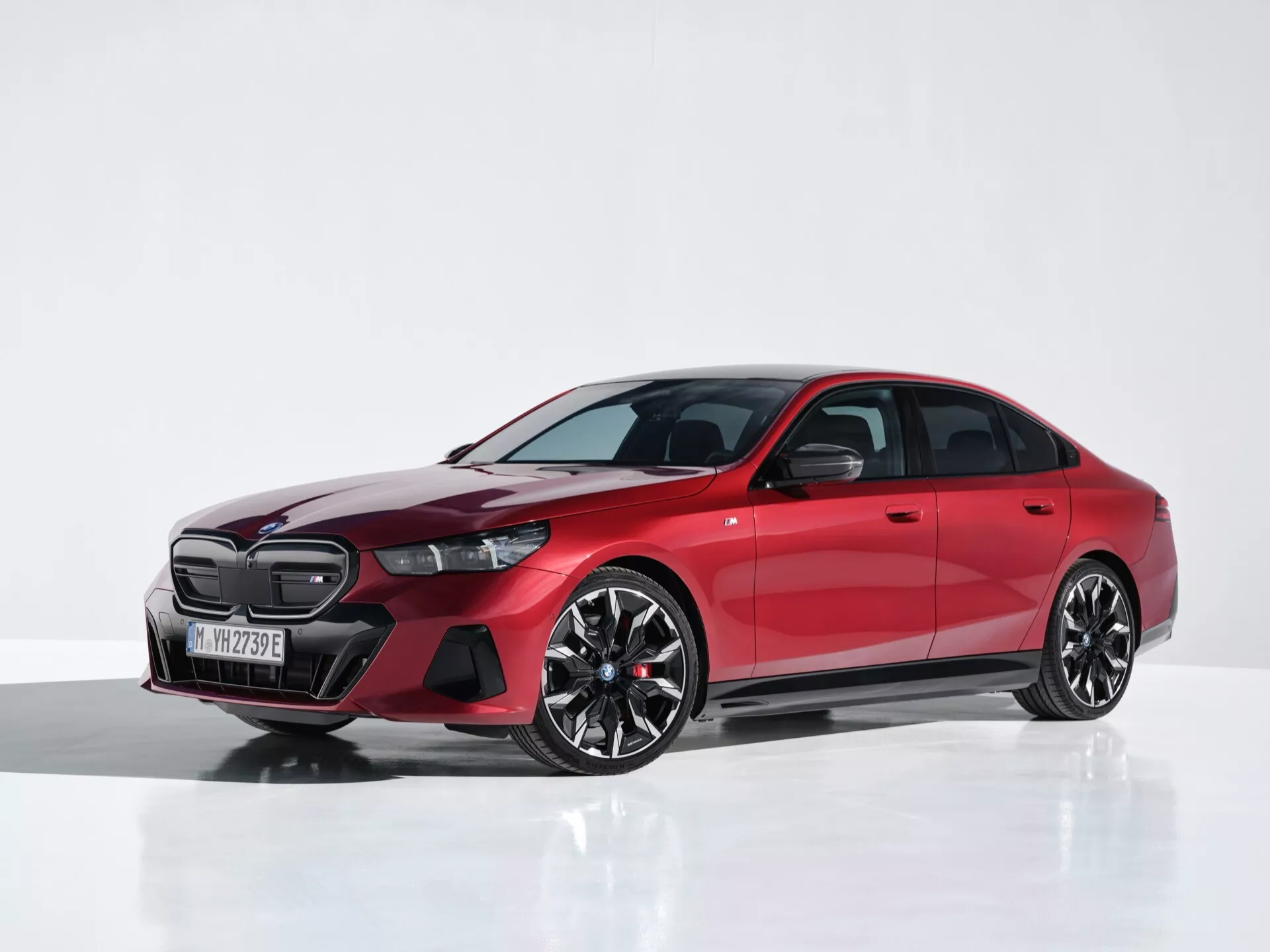 Rdeča BMW serija 5 (G60-G61) letnik 2023, srednji posnetek v studiu prikazuje LED žaromete, veliko sprednjo masko, aerodinamična lita kolesa in pnevmatike z nizkim profilom iz treh četrtin sprednjega pogleda