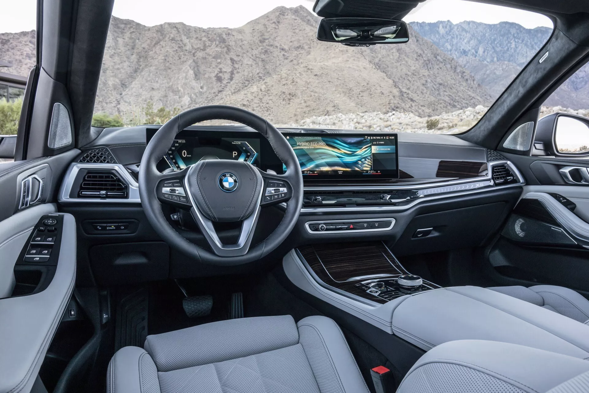 Pogled na notranjost iz zadnjih sedežev BMW X5 2023 (G05-F95-Facelift), ki prikazuje armaturo, volan, sredinsko konzolo in sprednje sedeže, opremljene z moderno tehnologijo in luksuznim dizajnom