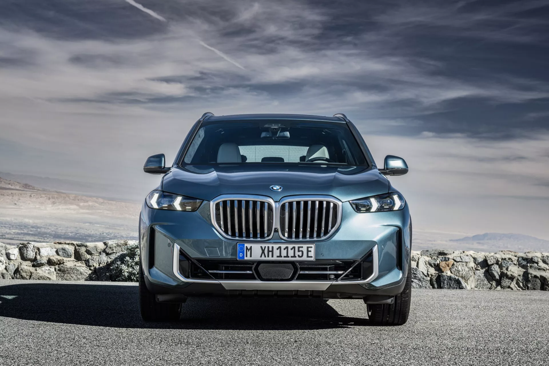 Sprednji pogled iz nizkega kota na model BMW X5 2023, ki prikazuje značilno ledvično rešetko, LED žaromete in aerodinamično zasnovo, z modrim poudarkom, ki nakazuje na elektrifikacijo
