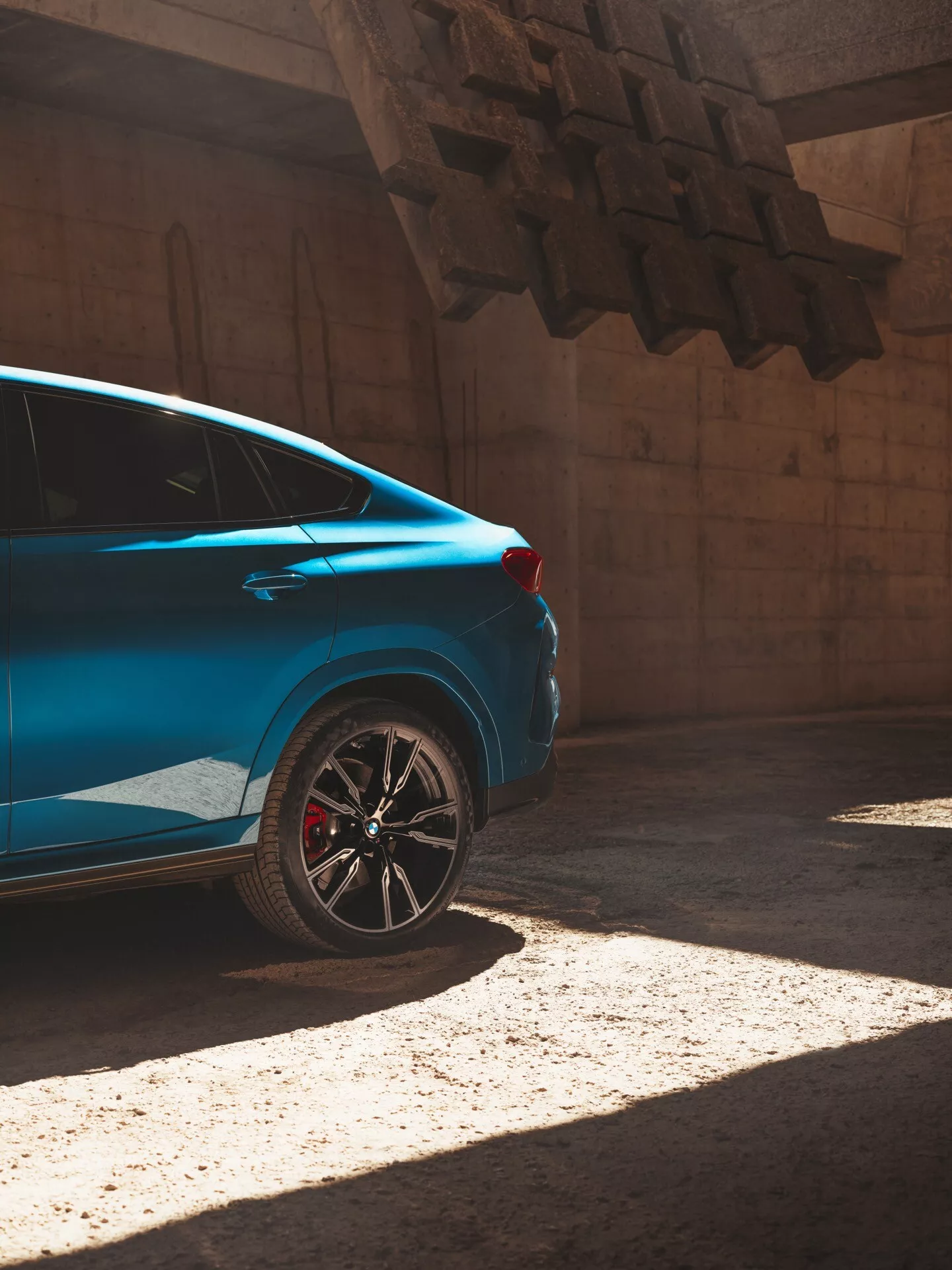 Modri avtomobil BMW X6 2023 (G06/F96 prenova) na soncu, pogled z zadnjega dela iz treh četrtin, ki poudarja zadnji del z športnim obročem in rdečo zavorno čeljustjo.