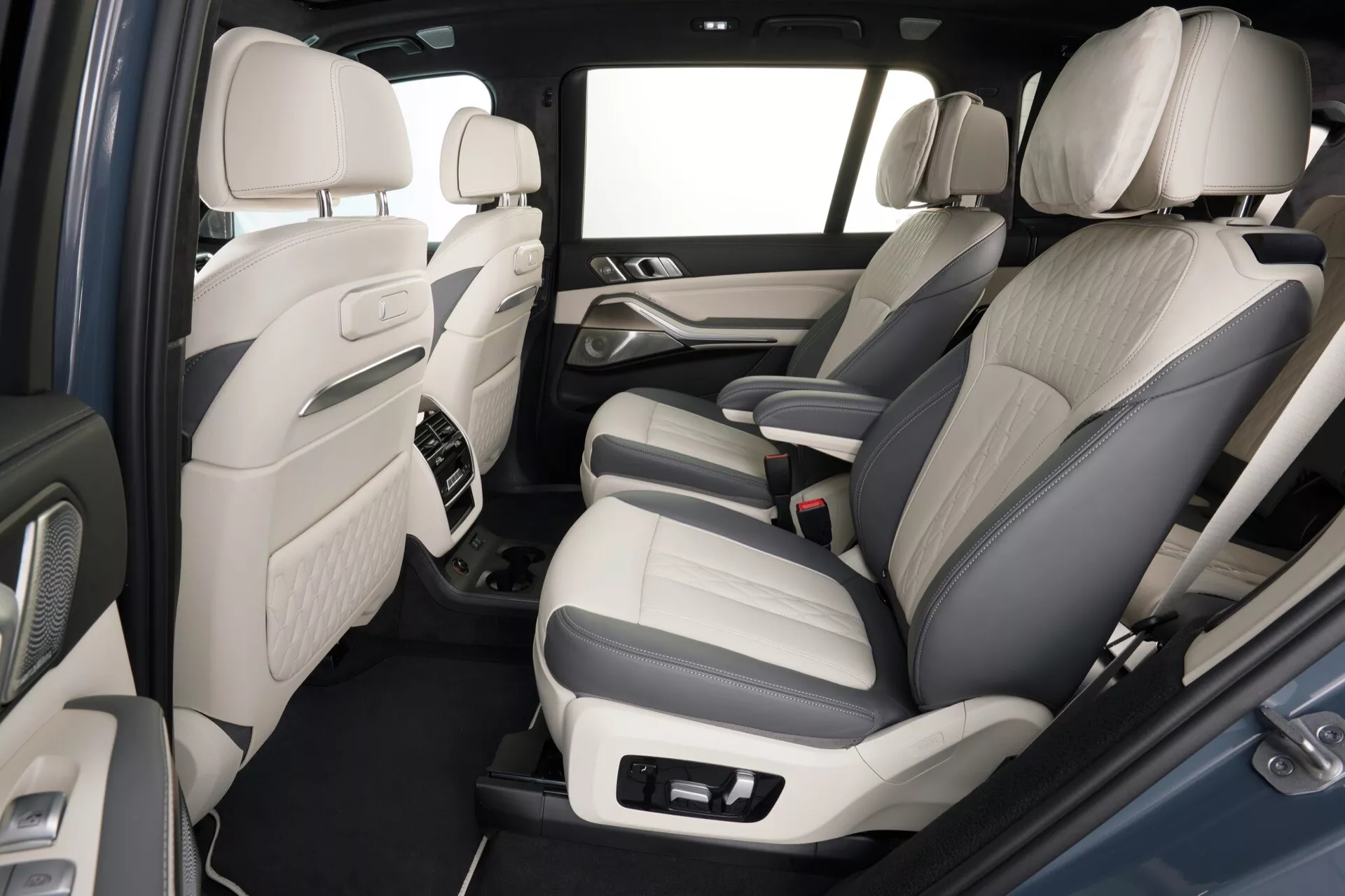 Notranji pogled na BMW X7 (G07 Facelift) za leto 2022, ki poudarja zadnji potniški del, z dvobarvno usnjenimi sedeži, naprednimi nadzornimi ploščami zvočnega sistema na vratnih panelih, sredinsko konzolo z akcenti iz kakovostnih materialov, preprogo na tleh, obilico prostora za noge in svetlo barvno shemo notranjosti za občutek prostrane kabine