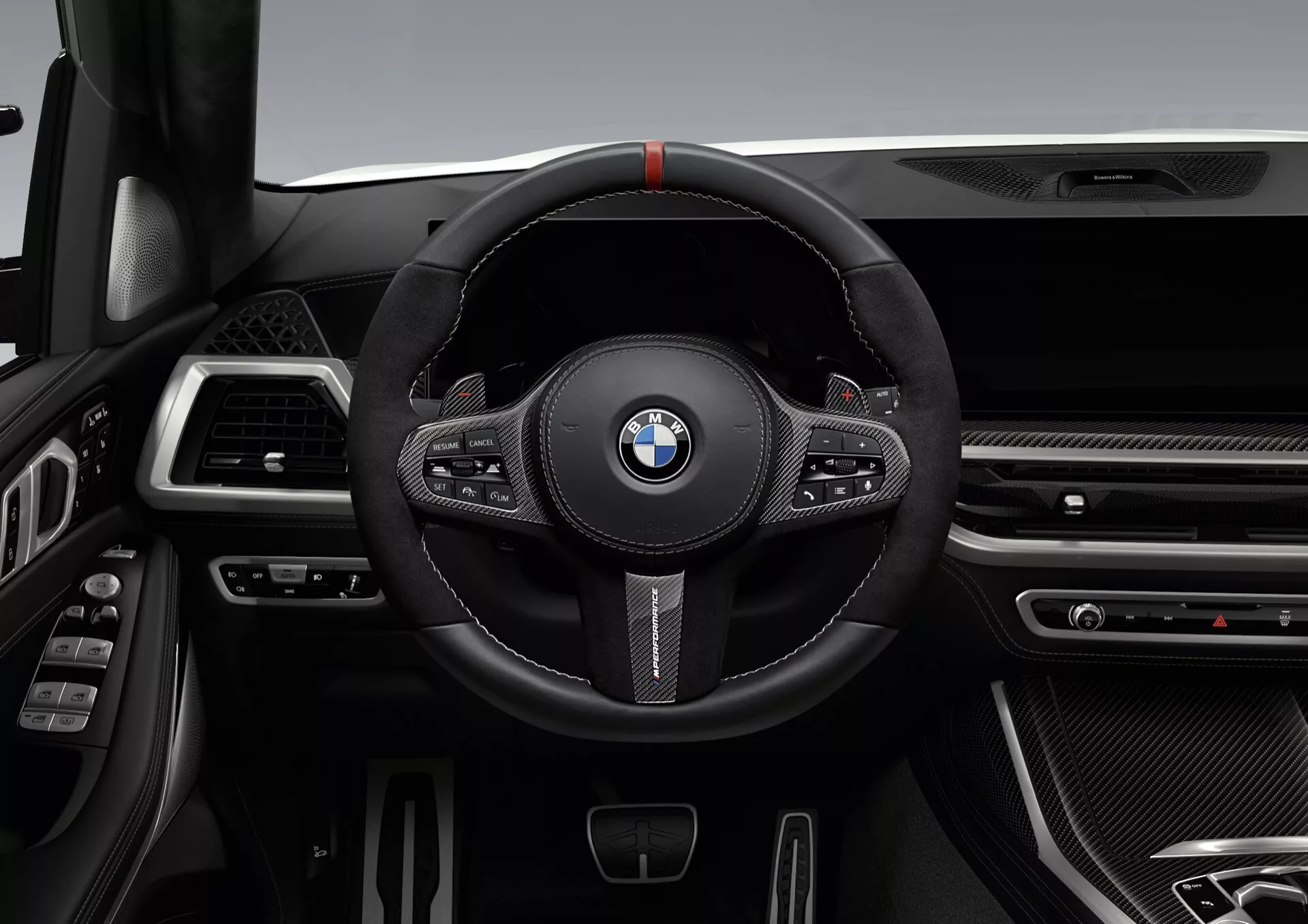 Notranjost BMW X7 2022 (G07-Facelift) s poudarkom na športnem volanu, oblečenem v črno usnje z rdečo oznako, multifunkcijskimi gumbi in veslaškimi prestavnimi ročicami v ozadju proti sofisticirani armaturni plošči s tankimi zračniki, kromiranimi in teksturami, ki spominjajo na ogljikova vlakna