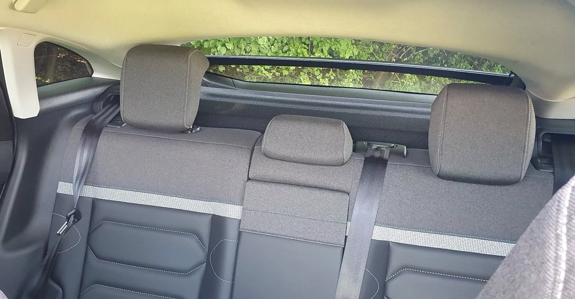 Notranjost Citroëna C4 2020, osredotočena na zadnje sedeže, gledano iz prednjih sedežev. Zadnja klop, razdeljena na tri dele z 60/40 funkcijo zlaganja, sprejme do treh potnikov. Tkaninska oblazinjena nakazuje na standardno raven opreme, z nastavljivimi vzglavniki za zunanje sedeže. Barvna shema je dvobarvna, z vidnimi plastičnimi elementi na straneh in ohišji varnostnih pasov. Napredna tehnologija ni vidna, vendar so prisotne standardne varnostne funkcije, kot so varnostni pasovi.