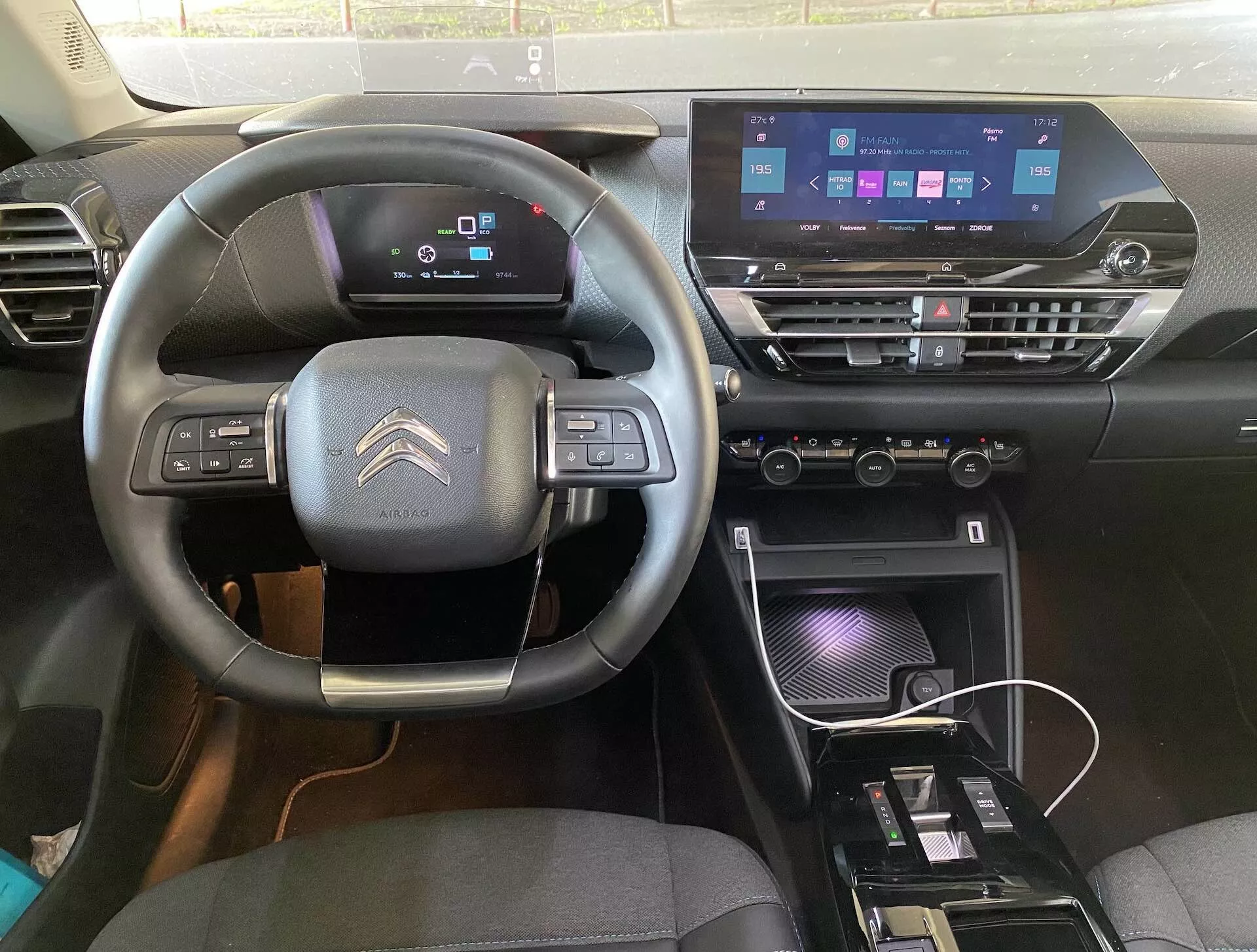 Notranji pogled Citroëna C4 2020 (e-C4) iz voznikovega sedeža, prikazuje volan s tremi kraki z vgrajenimi kontrolami, digitalno armaturno ploščo in moderno sredinsko konzolo z zaslonom na dotik infotainment sistema, krmilnimi enotami za klimo in polnilno območje.