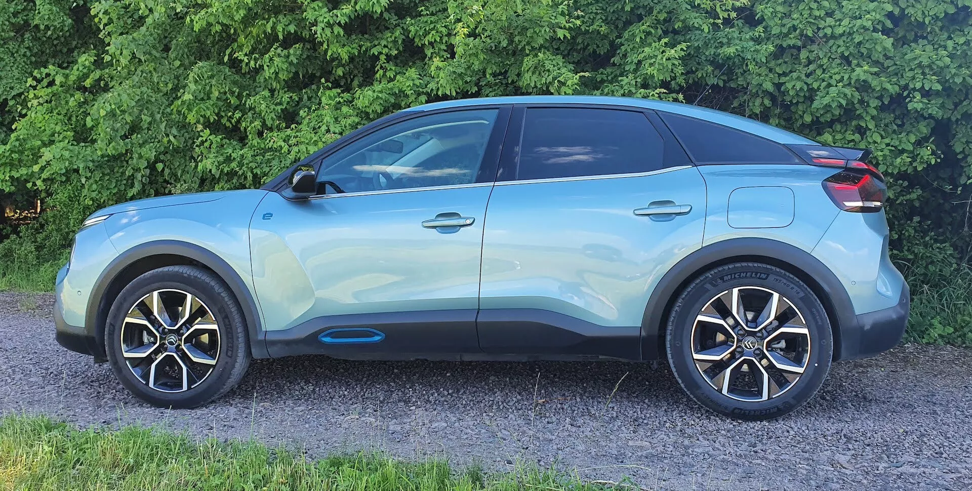Stranski profilni pogled na sodoben crossover/SUV Citroen C4 (e-C4) iz leta 2020. Svetlo modro vozilo je fotografirano s stransko-sprednjega kota, ki poudarja podrobnosti, kot so sijoča končna obdelava, lita platišča, stranska ogledala v barvi karoserije, drzne linije, črna obroba oken, zatemnjena zadnja stekla, ročaji vrat v ravnini karoserije z brezkontaktnim vstopom in strešna linija, ki se znižuje proti zadku, z možnim strešnim spojlerjem in nosilci. Na sliki so jasno vidna sprednje kolo in blatnik, prednja maska, odbijač in žarometi pa niso vidni.