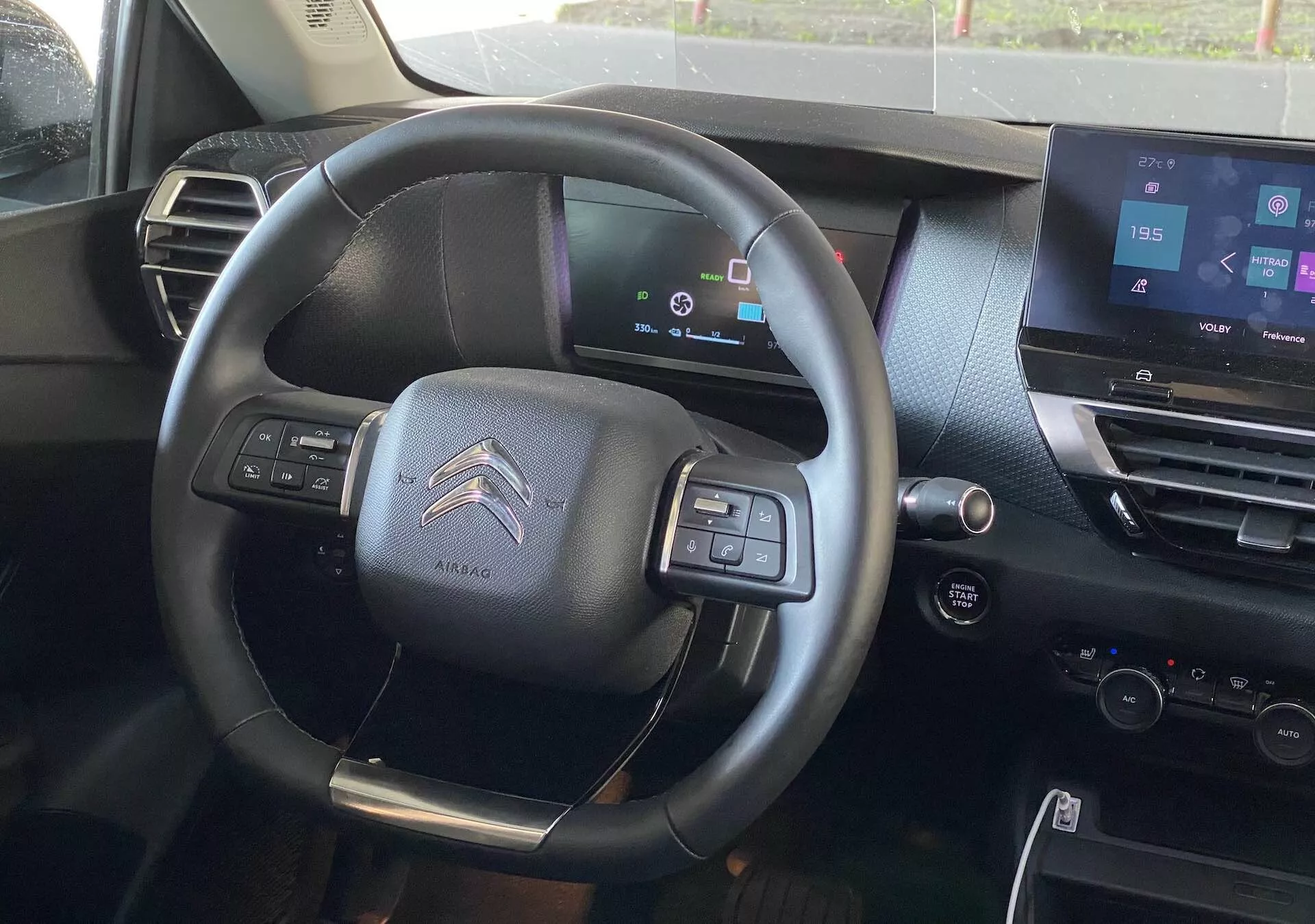 Notranji pogled Citroëna C4 2020 (e-C4) s voznikovega sedeža, s poudarkom na trikraki večfunkcijski volanski gredi s priložitvijo zračnih blazin, digitalno armaturno ploščo, ki prikazuje stanje vozila, zaslonom na dotik za informacijsko-razvedrilni sistem v sredinski konzoli, notranjim oblikovanjem v temnih tonih, kontrolnimi gumbi za avdio in telefonsko povezljivostjo, prestavnimi ročicami, ki nakazujejo polavtomatski menjalnik in kontrolnimi gumbi na vratih voznika za električna okna in nastavitev ogledal.
