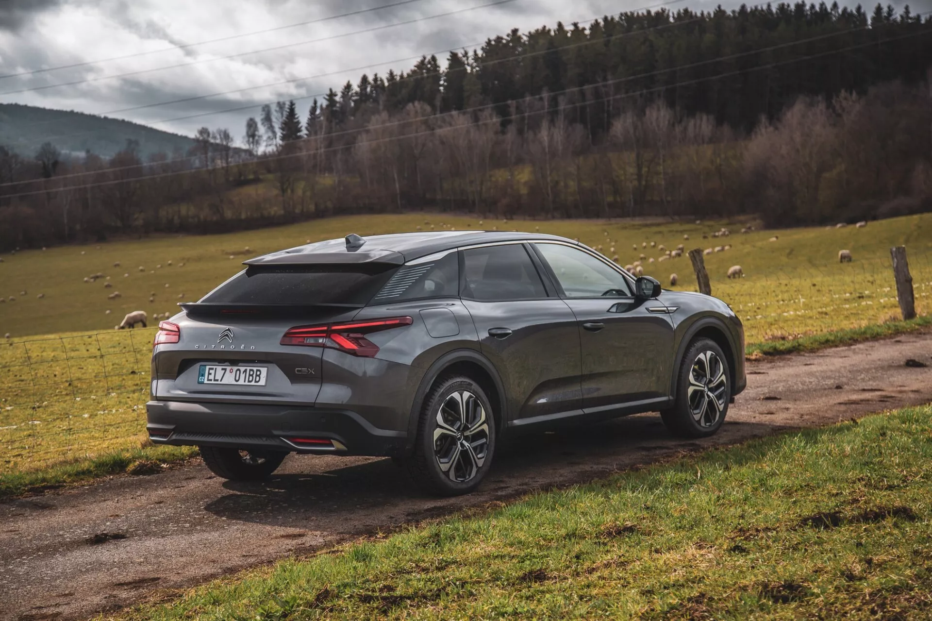 Citroen C5-X sodoben crossover SUV parkiran na prostem, pogled zadaj treh četrtin, ki poudarja LED zadnje luči, zadnji difuzor, senzorje za parkiranje ali kamero, anteno v obliki morskega psa, dvobarvna lita kolesa, poševno zadnje okno, integriran spojler in kovinsko obdelavo, nastavljeno proti naravnemu ozadju