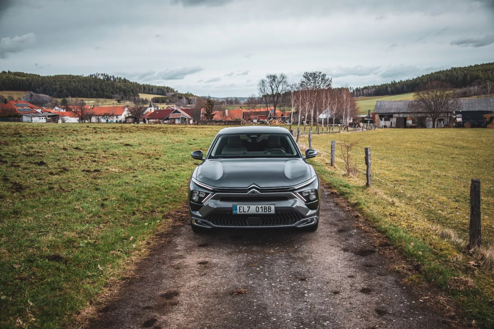 Čelni pogled na Citroën C5-X 2022 na ozkem pohodu v travniku pod oblačnim nebom, ki prikazuje svoj elegantni dizajn, zapleteno rešetko z emblemo, kotne LED žaromete, kiparske linije pokrova in dodatne sprednje svetlobne elemente, registrirano v Češki republiki.