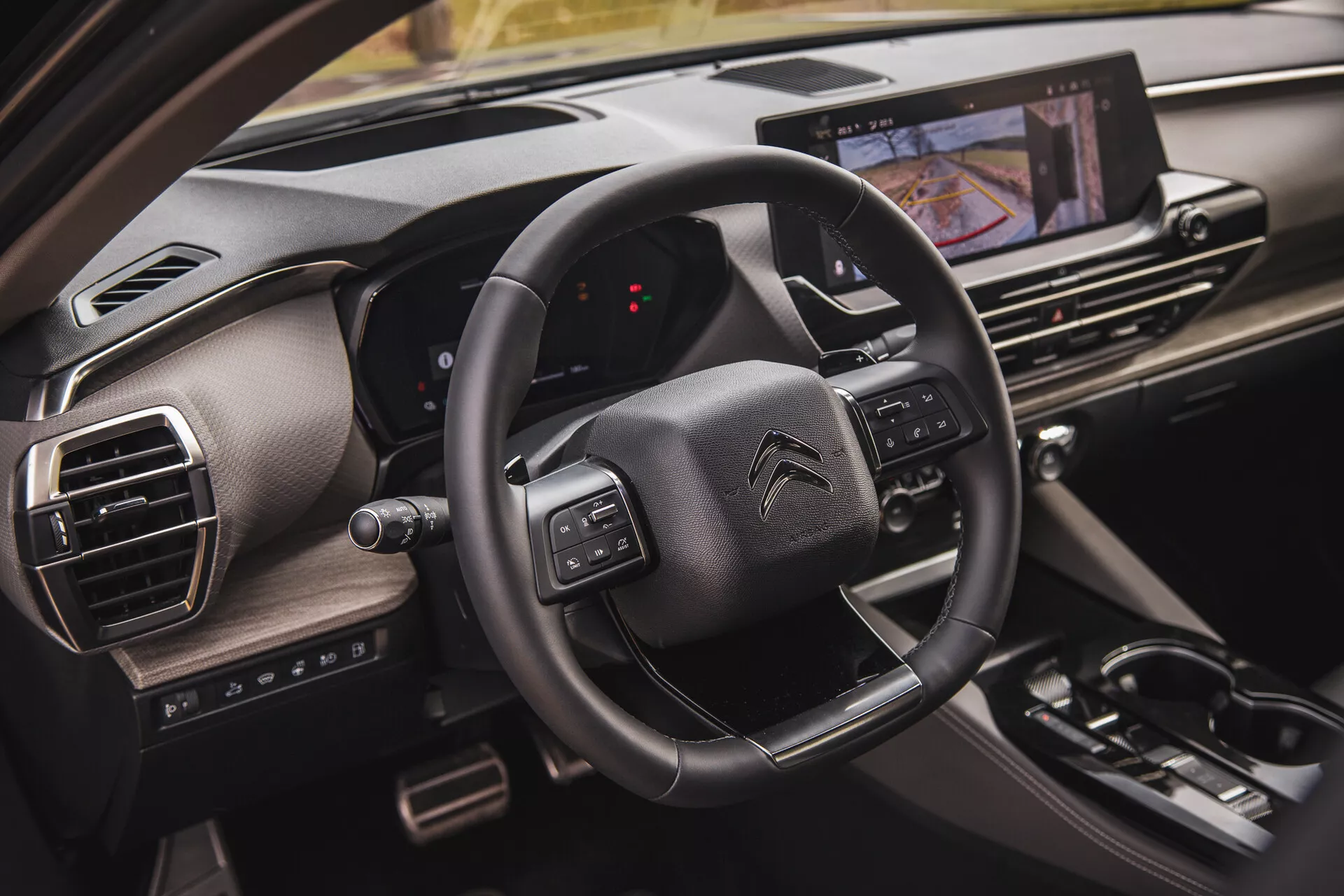 Pogled od blizu notranjosti Citroëna C5-X 2022, ki prikazuje volan z večfunkcijskimi gumbi, digitalno nadzorno ploščo z vidika sopotnika in zaslon na dotik za informacijsko-zabavni sistem