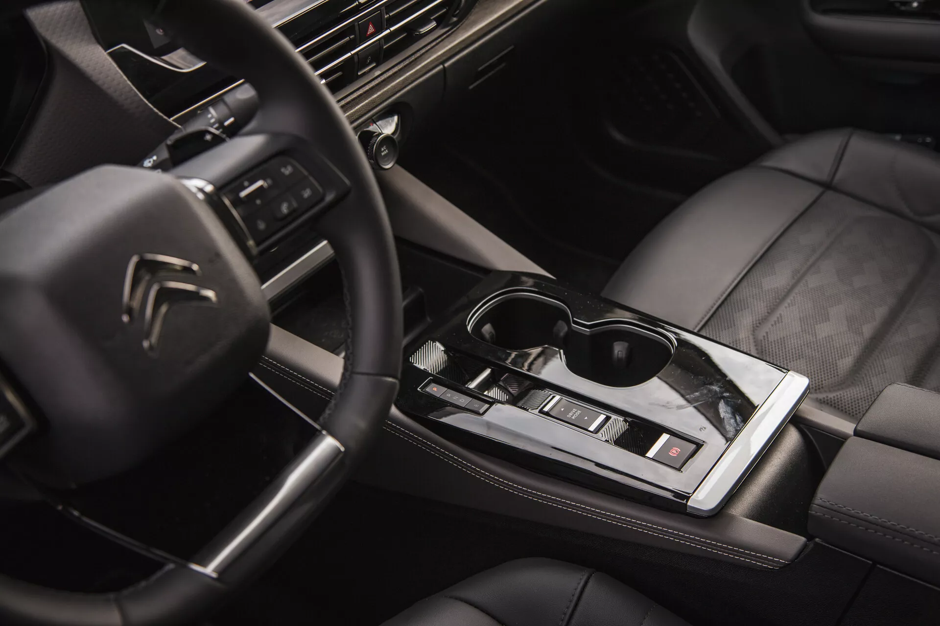 Notranji pogled Citroën C5-X 2022 z multifunkcijskim volanom z logotipom, visokotehnološko armaturno ploščo z infotainment sistemom, elegantno avtomatično prestavno ročico, klimatsko kontrolo, sedeži oblečeni v usnje z kvalitetnim šivanjem in pridih življenjskega sloga z sončnimi očali na srednji sijoči površini
