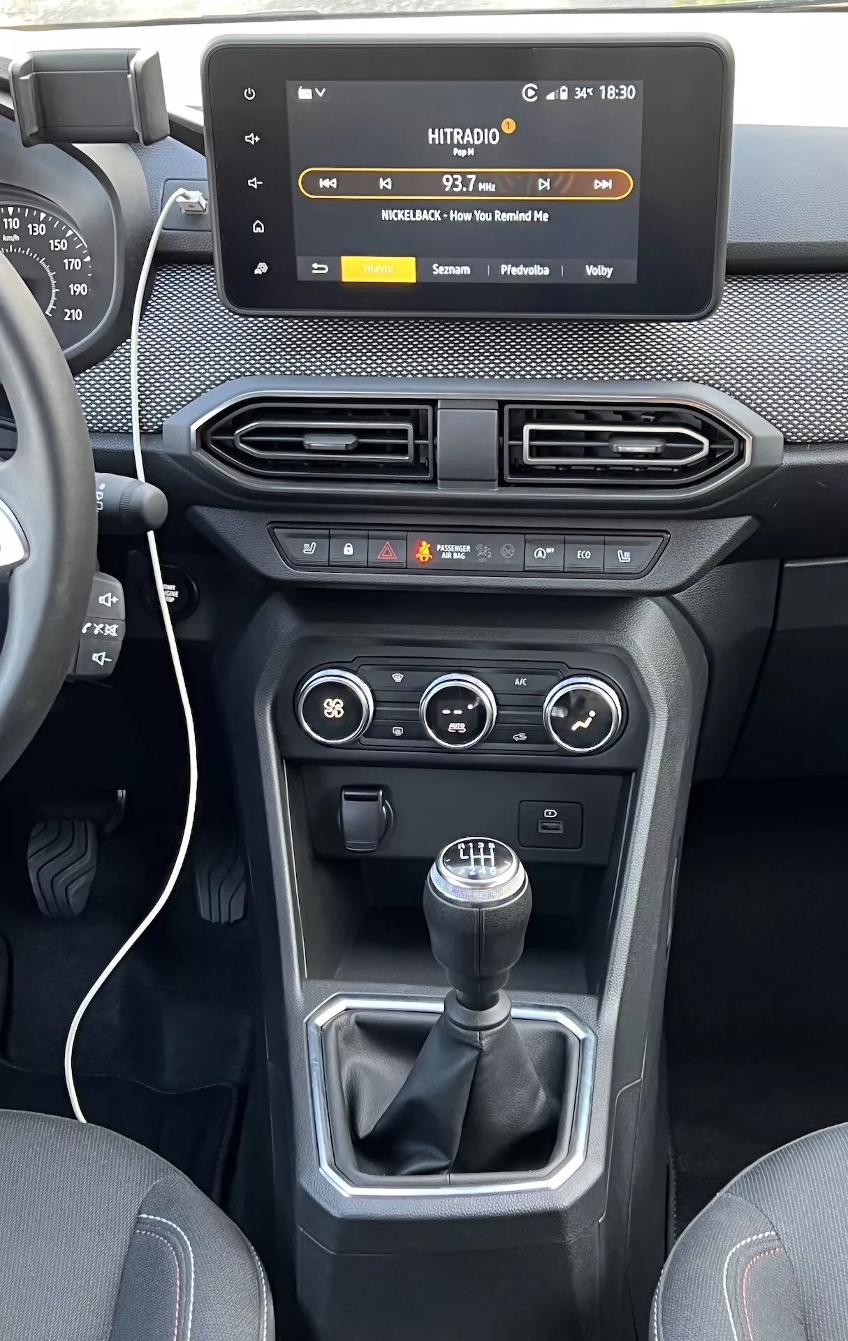 Pogled na notranjost Dacia Jogger 2022 usmerjen na sredinsko konzolo in armaturno ploščo, z značilnostmi plavajočega zaslona na dotik za infotainment, zračniki, kontrolniki klime in vozila ter ročnim menjalnikom