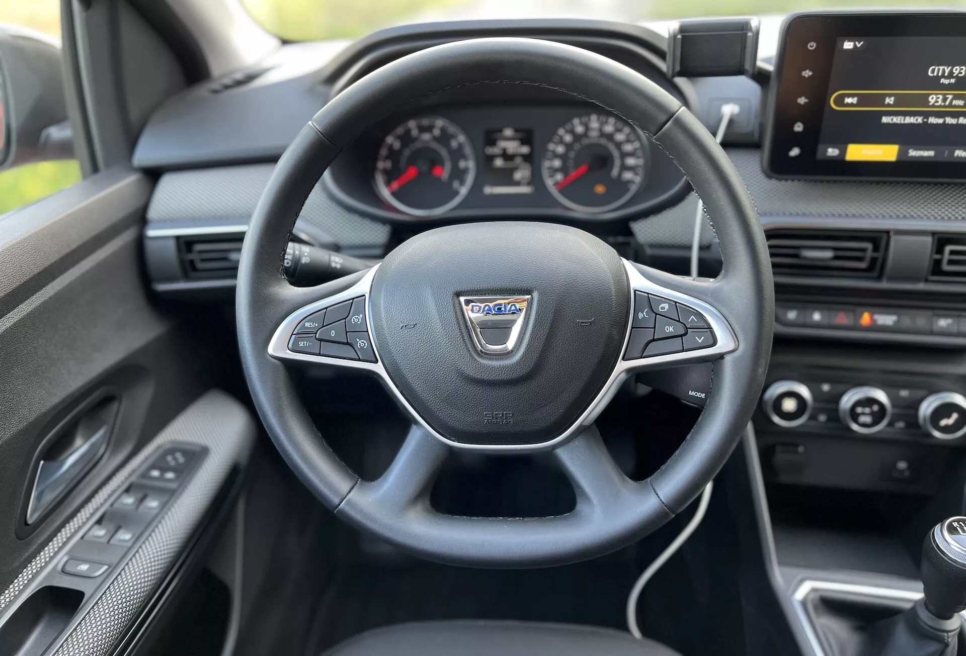 Notranji pogled na Dacia Jogger 2022 iz sedeža voznika, ki prikazuje večfunkcijski volan, ovit v usnje, analogni instrumentni sklop s centralnim digitalnim zaslonom, zaslon za infotainment, klimatsko kontrolo in ročico ročnega menjalnika