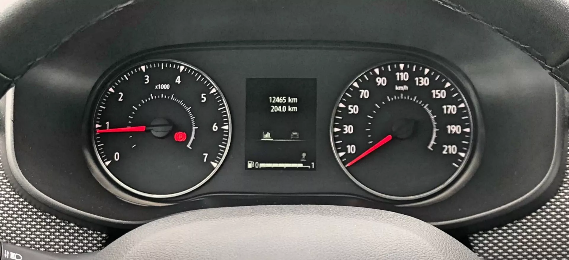 Pogled od blizu Dacia Sandero-Stepway 2020 instrumentne plošče, ki prikazuje merilno ploščo z gladko, teksturirano armaturno ploščo. Analogni tahometer na levi strani, ki prikazuje hitrost motorja v RPM, in hitrostomer na desni strani, ki prikazuje hitrost vozila v km/h, oba s črnim ozadjem, belimi številkami in rdečimi kazalci. Digitalni prikazovalnik v sredini prikazuje kilometre prevoženih 17465 km in potovalni števec 2940 km.