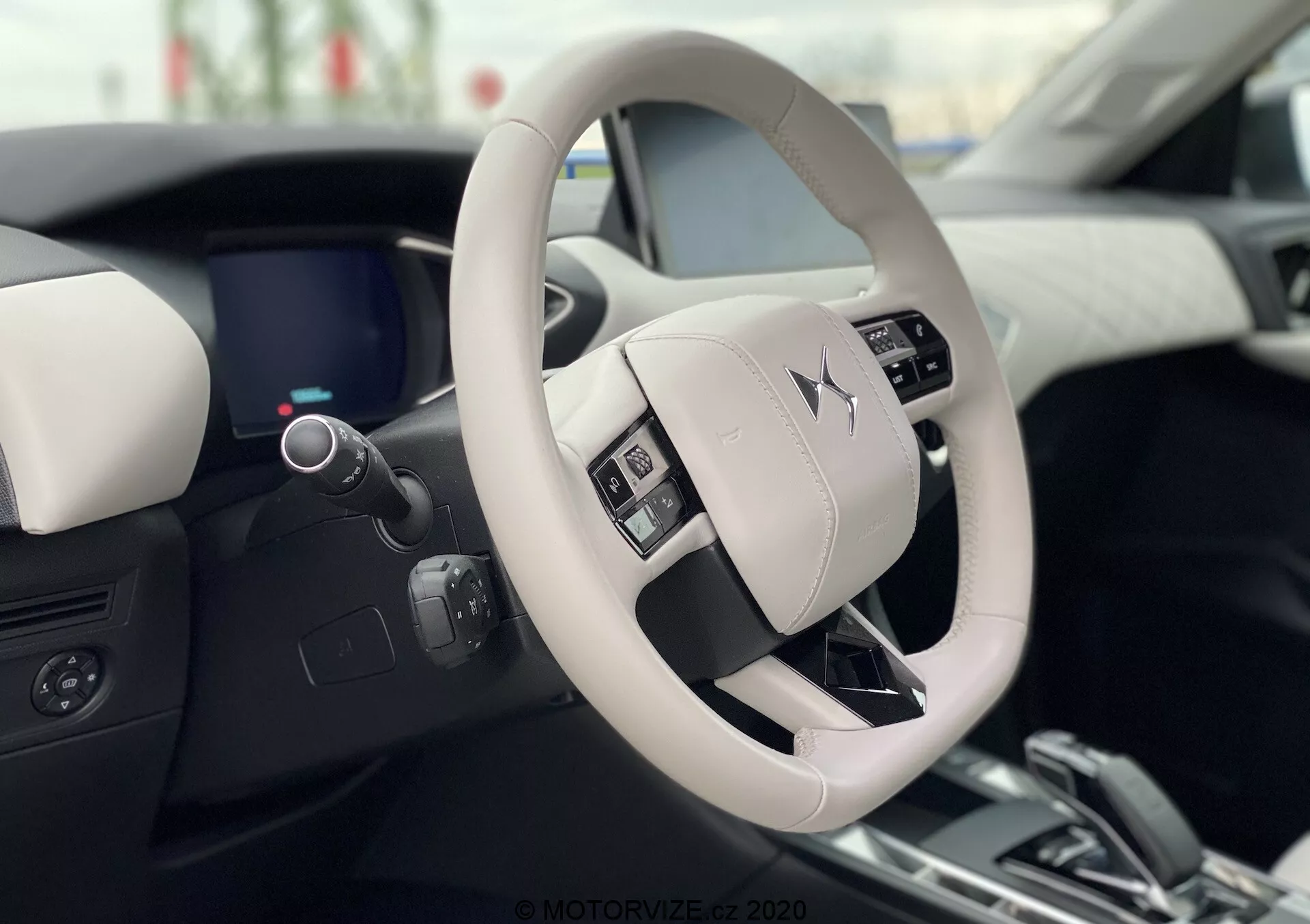 Notranji pogled na DS Automobiles DS 3 Crossback E-Tense 2019, ki prikazuje moden in razkošen dizajn volana in armaturne plošče iz perspektive vozniškega sedeža. Svetlo obarvan volan ima nadzorne gumbe in prikazuje logotip proizvajalca. Elegantna digitalna armaturna plošča, delno vidna za volanom, dopolnjuje dvobarvno notranjost z visokokakovostnimi materiali.