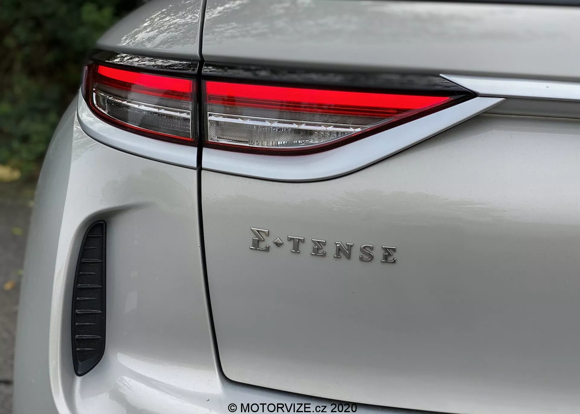 Bližnji posnetek zadnjega dela sodobnega srebrnega DS Automobiles DS 3 Crossback E-Tense 2019, ki prikazuje elegantno vodoravno LED zadnjo luč, značko E-TENSE na pokrovu prtljažnika in sijoč lak z odsevi. Viden oblikovni element ali odprtina za prezračevanje blizu kolesnega ohišja, poudarjajoč avtomobilski dizajn, tehnologijo in ekološke lastnosti.