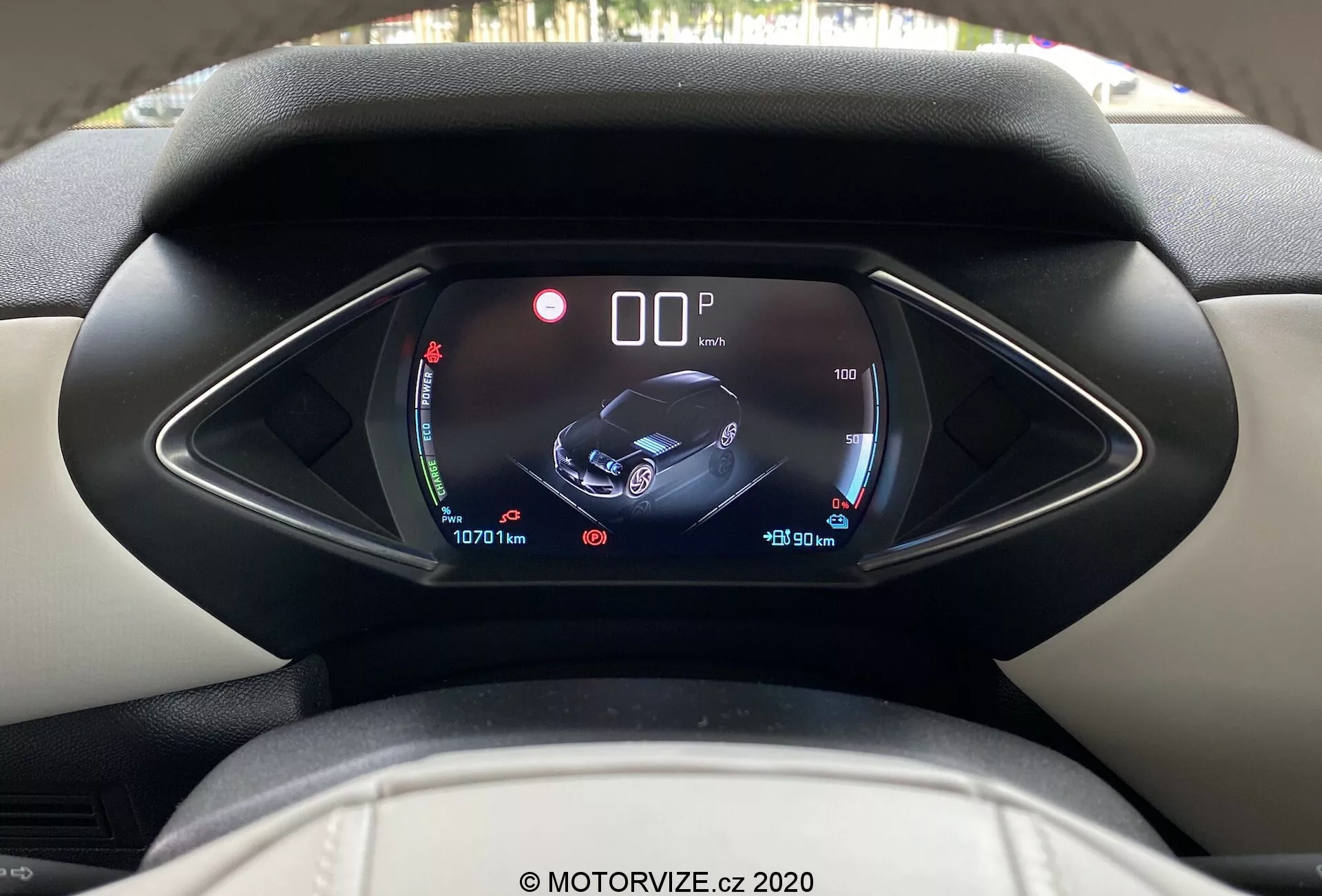 Pogled na notranjost vozila DS Automobiles DS-3 Crossback E-Tense iz leta 2019 iz voznikove perspektive, poudarja digitalni instrument z edinstveno asimetrično kapuco. Zaslon prikazuje kazalnika baterije in temperature, centralno grafiko vozila z ikonami za varnost in pomoč ter informacije o potovalnih podatkih in odčitanjih merilnika kilometrine, kar kaže na sodobne in visokotehnološke notranje značilnosti. Čista in jasna slika z vodnim žigom MOTORVIZE.cz 2020.