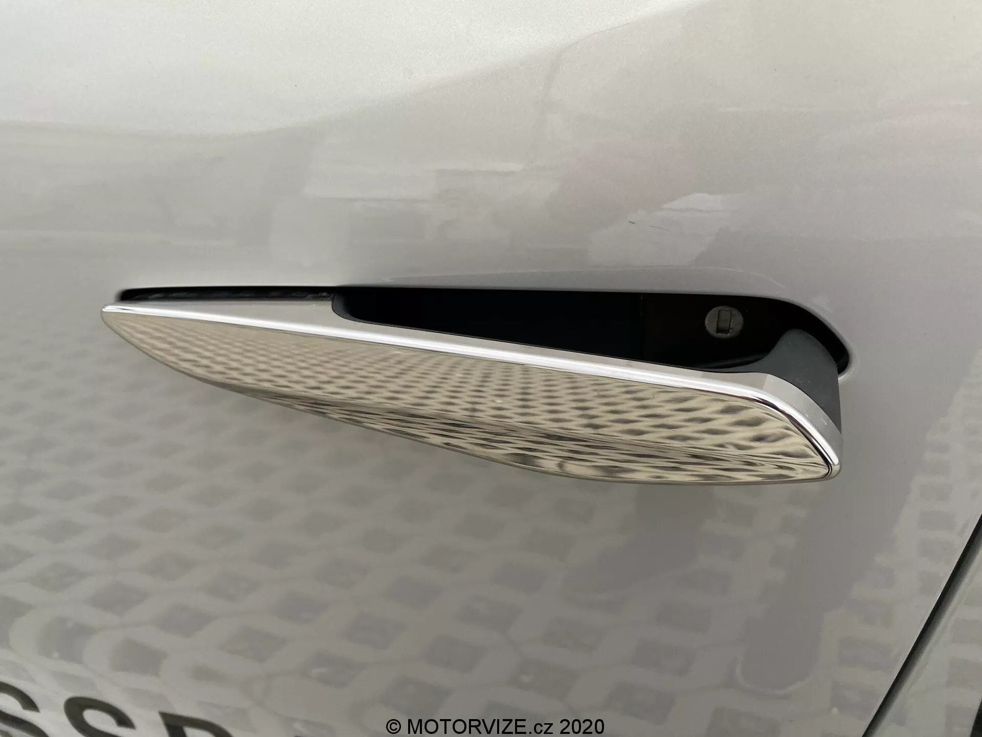Od blizu pogled na zračni reži avtomobila DS Automobiles DS-3 2019 (DS-3 Crossback E-Tense), s sijočim kromiranim zaključkom in značilnim valovitim vzorcem notranje mrežice, posneto iz stranskega kota z mehko osvetlitvijo za poudarjanje krivulje in oblikovalskih elementov na površini karoserije.