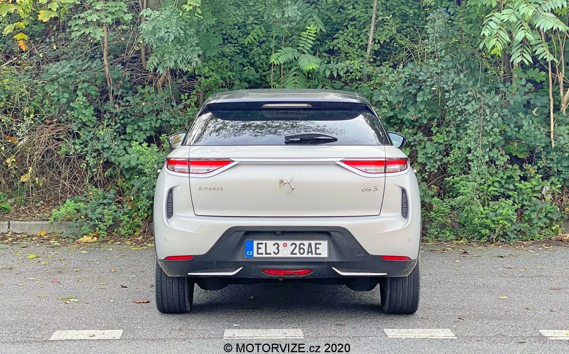 Slika prikazuje zadnji pogled na DS Automobiles DS 3 Crossback E-Tense iz leta 2019, fotografirano na višini oči s poudarkom na zadnji strani. Vidne značilnosti vključujejo centrirano registrsko tablico, oznake znamke in modela na prtljažniku, sodobne horizontalno usmerjene zadnje luči z zapletenimi LED vzorci, zadnje steklo z brisalcem, strešni spojler in odbijač z odsevnim trakom. Tradicionalne izpušne cevi niso vidne, kar nakazuje, da gre za električno vozilo. Dizajn je čist, verjetno vključuje napredne tehnološke značilnosti, značilne za električne ali hibridne avtomobile.