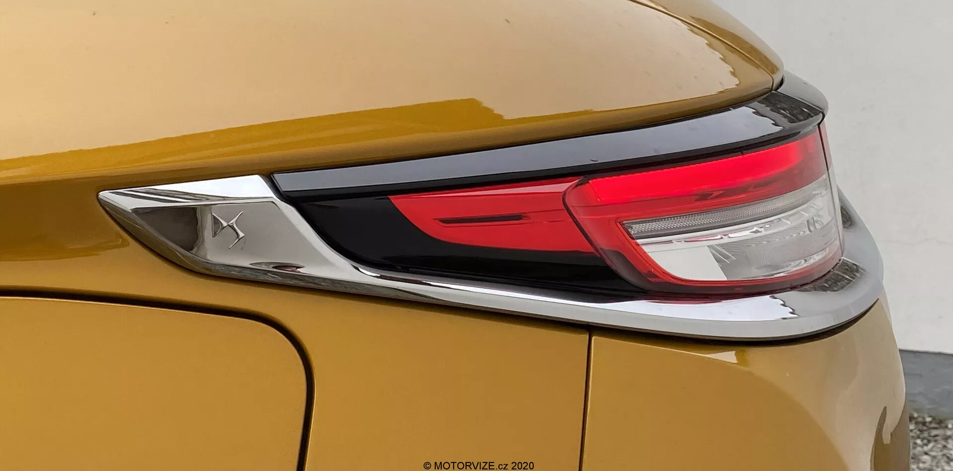 Bližnji pogled na zadnji del avtomobila DS Automobiles DS-3 2019 (DS-3 Crossback). Slika se osredotoča na desni del vozila, prikazuje kovinsko zlato ali bronasto karoserijo, del zadnjih LED luči in gladek, ukrivljen zadnji del z izrazito linijo. Viden je tudi kromiran emblem, vendar znamke ni mogoče prepoznati.