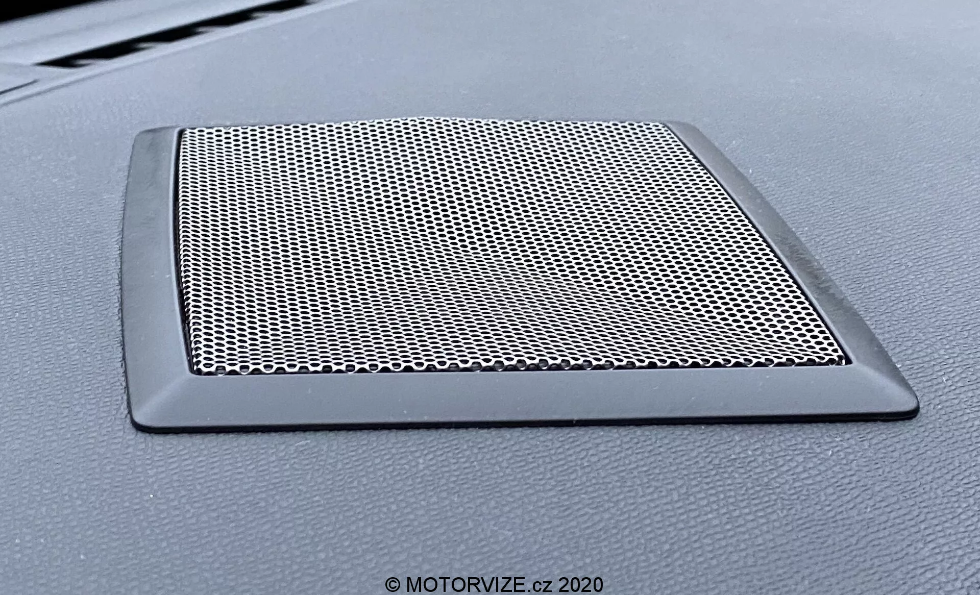 Pogled od blizu na mrežico zvočnika na armaturni plošči vozila DS Automobiles DS-3 Crossback model 2019. Trapezoidna mrežica z gosto tkano mrežo za zaščito zvočnika in elegantnim, neodsevnima robom, ki se zlije z armaturno ploščo.