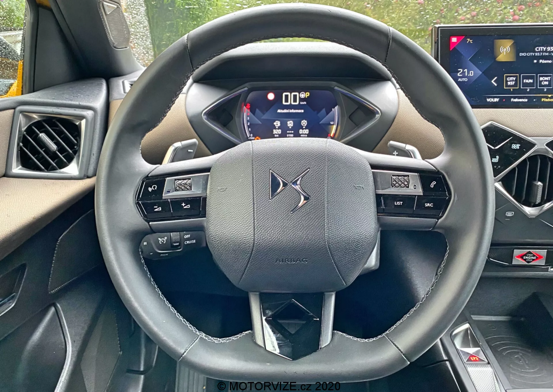 Perspektiva iz prve osebe iz voznikovega sedeža DS-Automobiles DS-3 2019 (DS-3 Crossback), osredotočena na volan s tremi kraki, obložen usnje in vgrajene kontrole ter obvočnice za prestavljanje. Digitalni instrumentni panel prikazuje ključne informacije, kar poudarja napredno tehnologijo vozila. Zaslon na dotik sistema za zabavo in informiranje na sredinski konzoli nakazuje visoke udobnostne funkcije vozila.