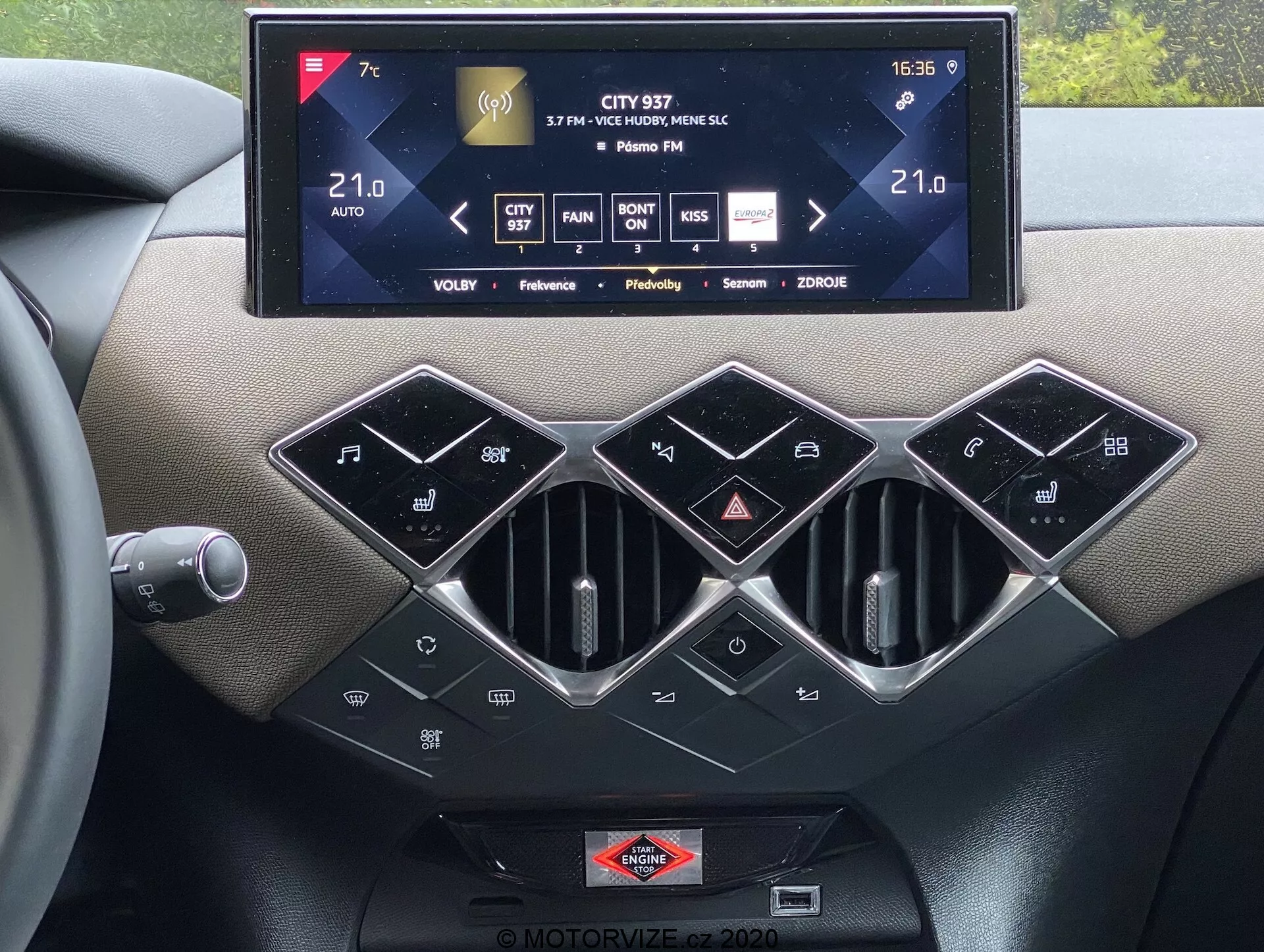 Notranji pogled na sredinsko konzolo ds-automobiles ds-3 2019 z velikim zaslonom na dotik sistema za informiranje in zabavo, ki prikazuje nadzor nad klimatskimi napravami, informacije o radiu in nastavitve, s tremi šesterokotnimi zračnimi šobami s srebrnim obročem spodaj. Obstaja vrsta sijočih črnih gumbov za nadzor klimatskih naprav, vključno s SYNC za nadzor klimatskih naprav za več območij, zmožnosti avtomatskega nadzora klimatskih naprav in značka blagovne znamke, nameščena pod zaslonom na dotik, poudarja vrhunske otipne materiale in sodobno avtomobilsko tehnologijo