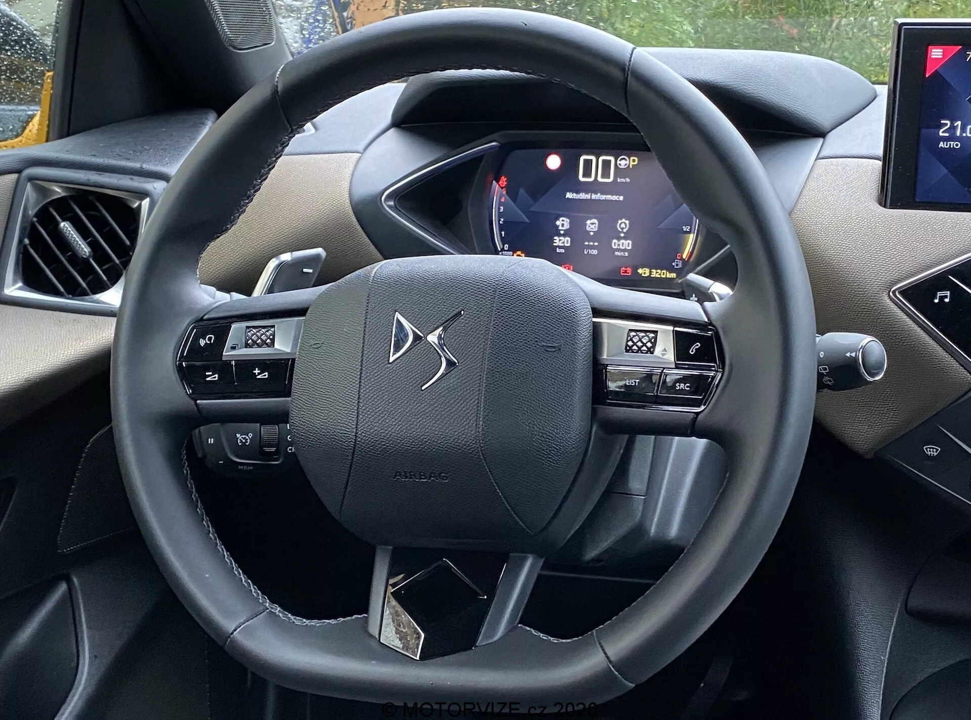 Notranji pogled avtomobila DS Automobiles DS-3 2019 (DS-3 Crossback) iz perspektive voznikovega sedeža, s volanom z gumbi za večmedijsko upravljanje, glasovne ukaze in verjetno nastavitve tempomata, aktivno digitalno instrumentno ploščo, ki prikazuje različne informacije o vozilu, in delom infotainment sistema s potencialno povezljivostjo pametnih telefonov in navigacijskimi zmogljivostmi. Notranjost vključuje kombinacijo mehke plastike in kromiranih poudarkov, ki prikazuje moderno tehnologijo in estetski videz.