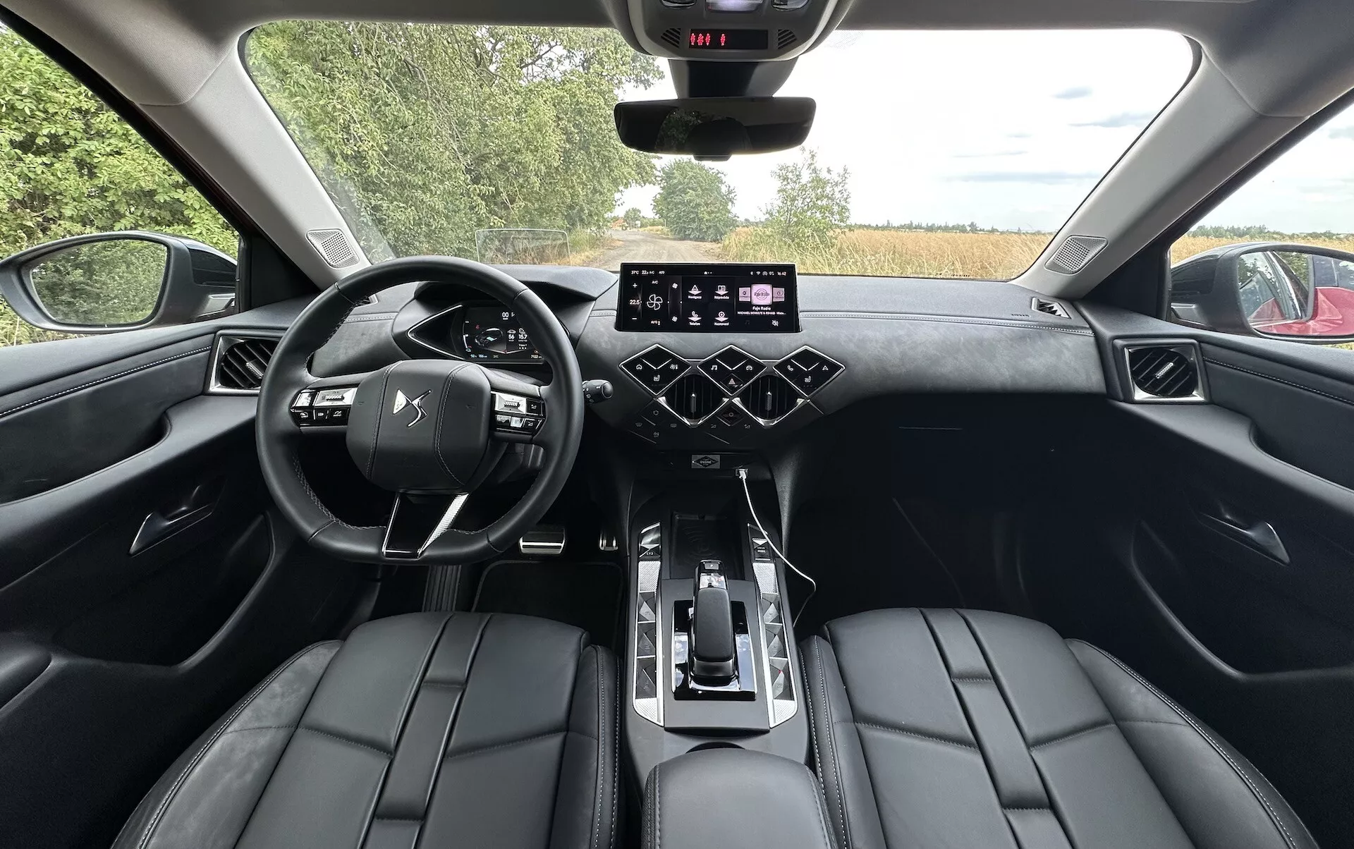 Pogled notranjosti DS Automobiles DS-3 2023 s zadnjega sedeža, ki prikazuje armaturno ploščo, digitalni instrumentni zaslon, multifunkcijski volan, zaslon na dotik za informacijsko-razvedrilni sistem, gumbe za nadzor klime in luksuzne usnjene sedeže.