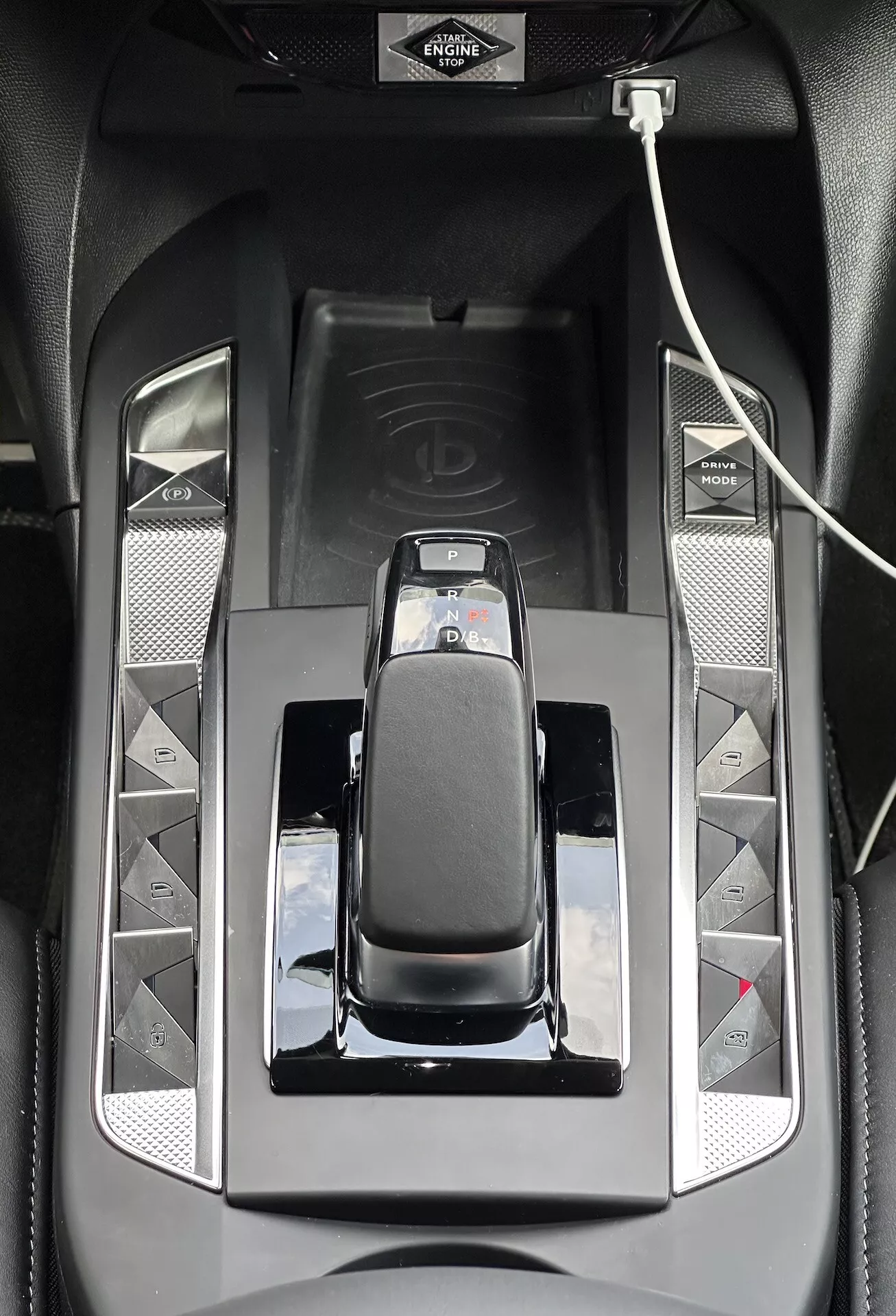 Pogled od blizu na sredinsko konzolo DS 3 E-TENSE 2023, ki prikazuje elegantno avtomatsko prestavno ročico s kromiranim robom, sijoče črne površine in gumbe za napredne funkcije vožnje