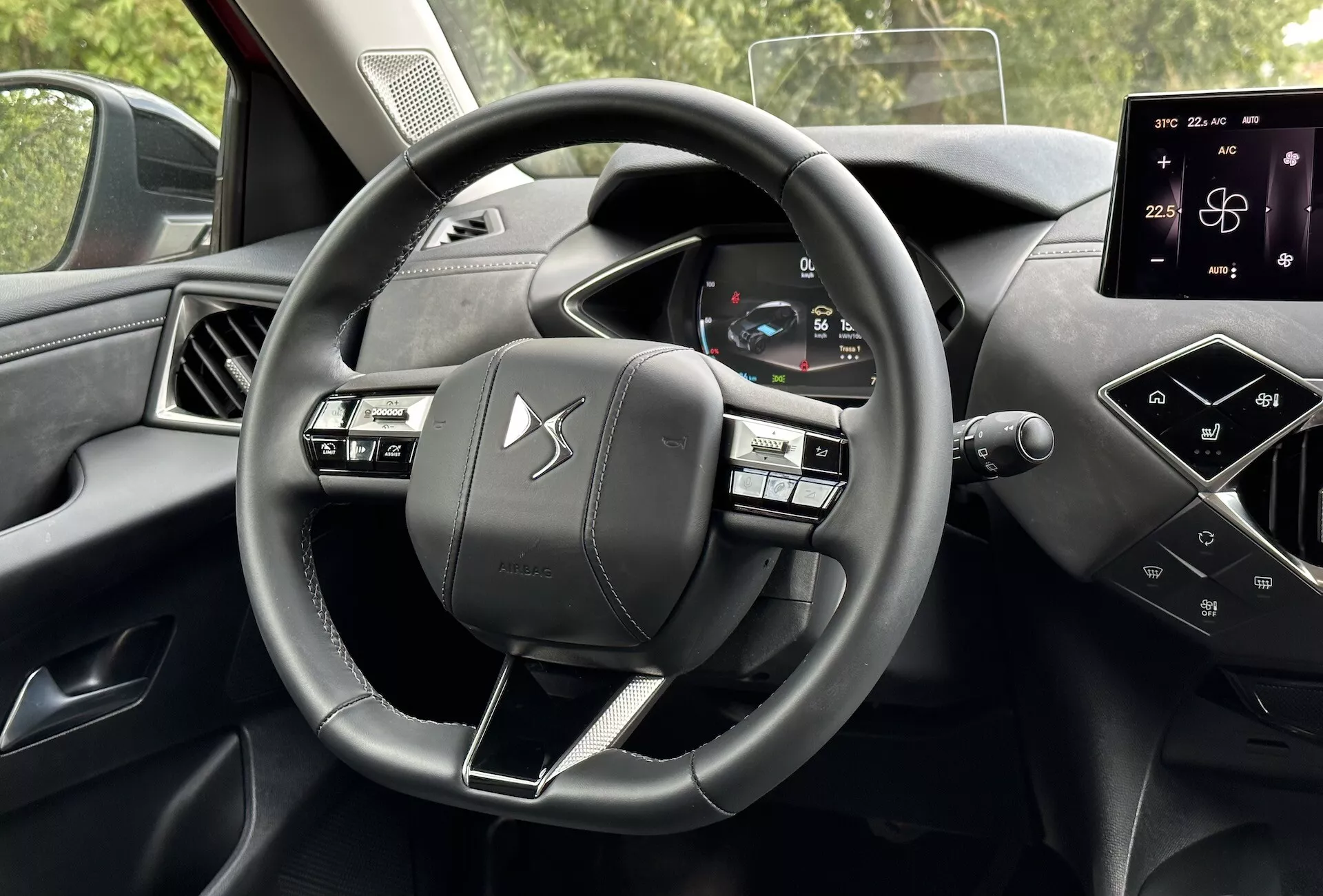 Pogled na notranjost DS Automobiles DS-3 2023 (DS-3 E-TENSE) iz perspektive voznika, ki poudarja volan s tremi kraki z multifunkcijskimi gumbi, digitalni instrumentni panel, ki prikazuje hitrost vozila in diagnostiko, in interaktiven zaslon na dotik na sredinski konzoli za navigacijo in nastavitve vozila, kar prikazuje sodobno avtomobilsko tehnologijo in elemente premijskega dizajna.