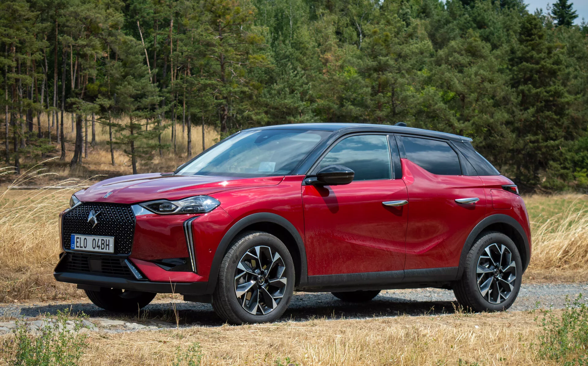 Stransko sprednji pogled na DS Automobiles DS 3 E-TENSE 2023, rdeči crossover SUV, lita kolesa z več kraki, LED žarometi, na gramozni poti z gozdnim ozadjem