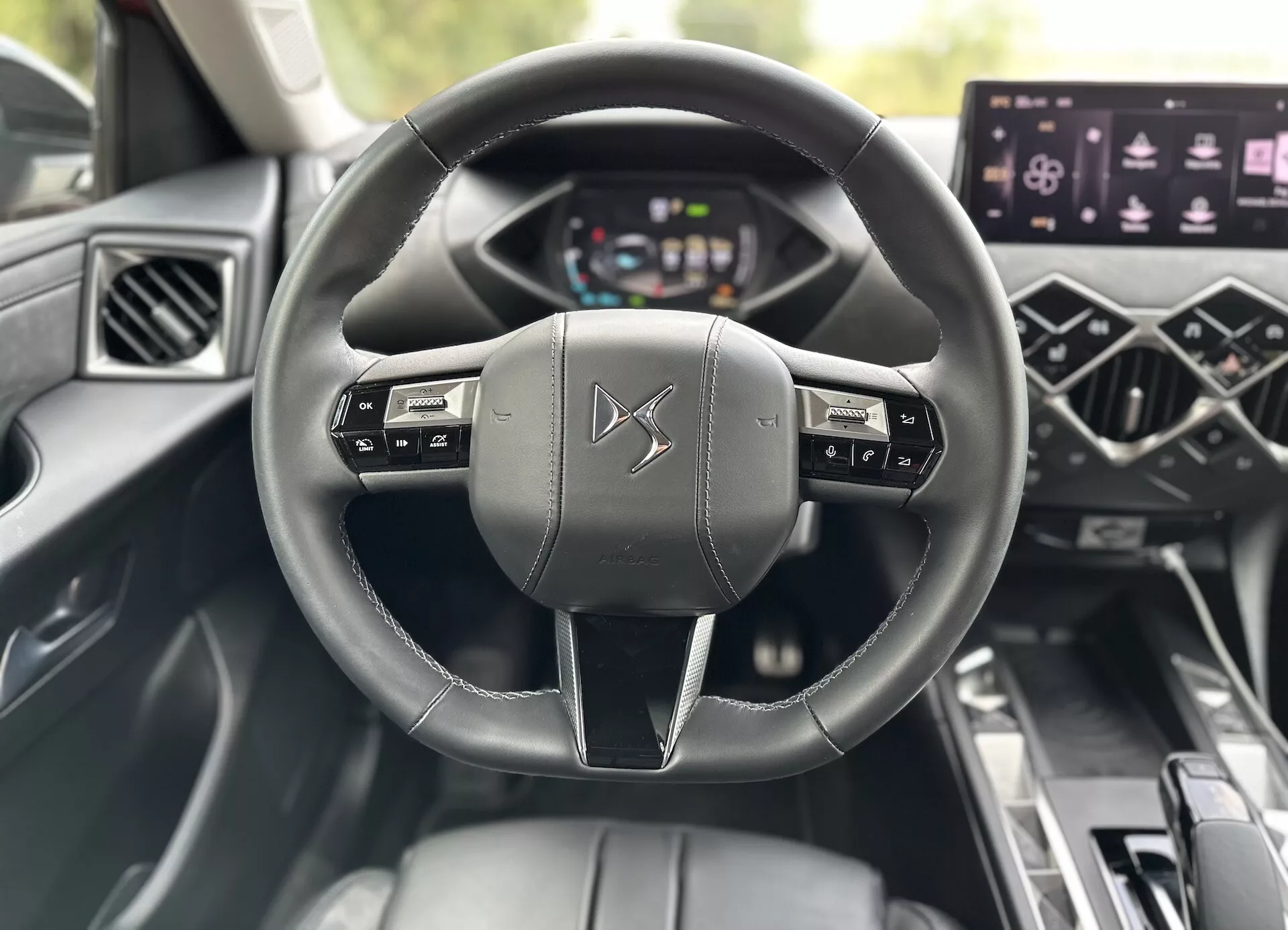 Notranji pogled DS 3 E-Tense 2023 s krmilnim obročem, ovitim z usnjem, z gumbi za upravljanje multimedijskih funkcij, digitalnim instrumentnim sklopom, sredinskim zaslonom na dotik za infotainment sistem in kontrolami za električna okna, poudarja napredno tehnologijo in dizajn luksuznega vozila