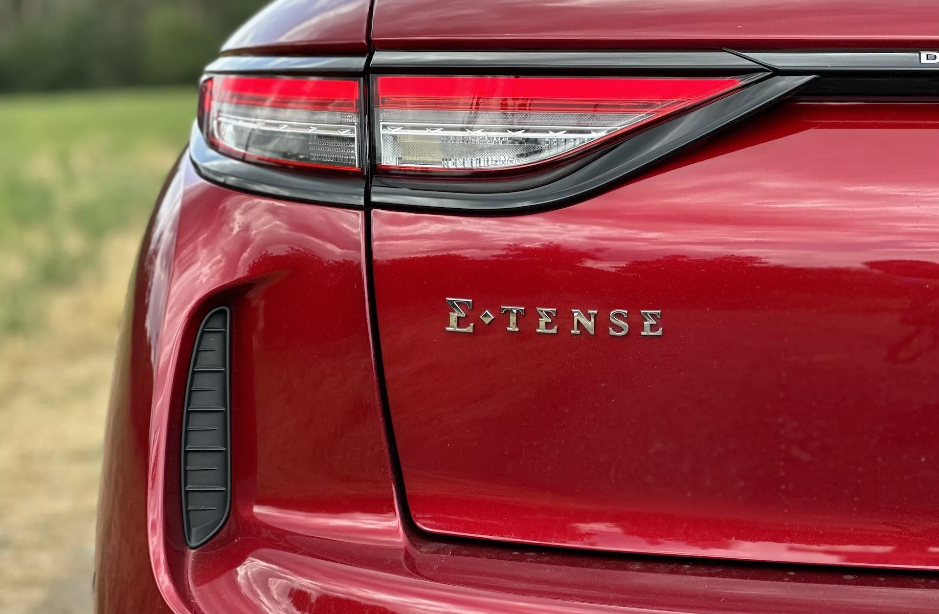 Podroben pogled na zadnjo levo stran DS Automobiles DS-3 E-TENSE 2023, kjer so izpostavljeni LED zadnja luč, oznaka E-TENSE, sijoča rdeča barva, zračnik in detajlna izdelava v naravnem zunanjem okolju