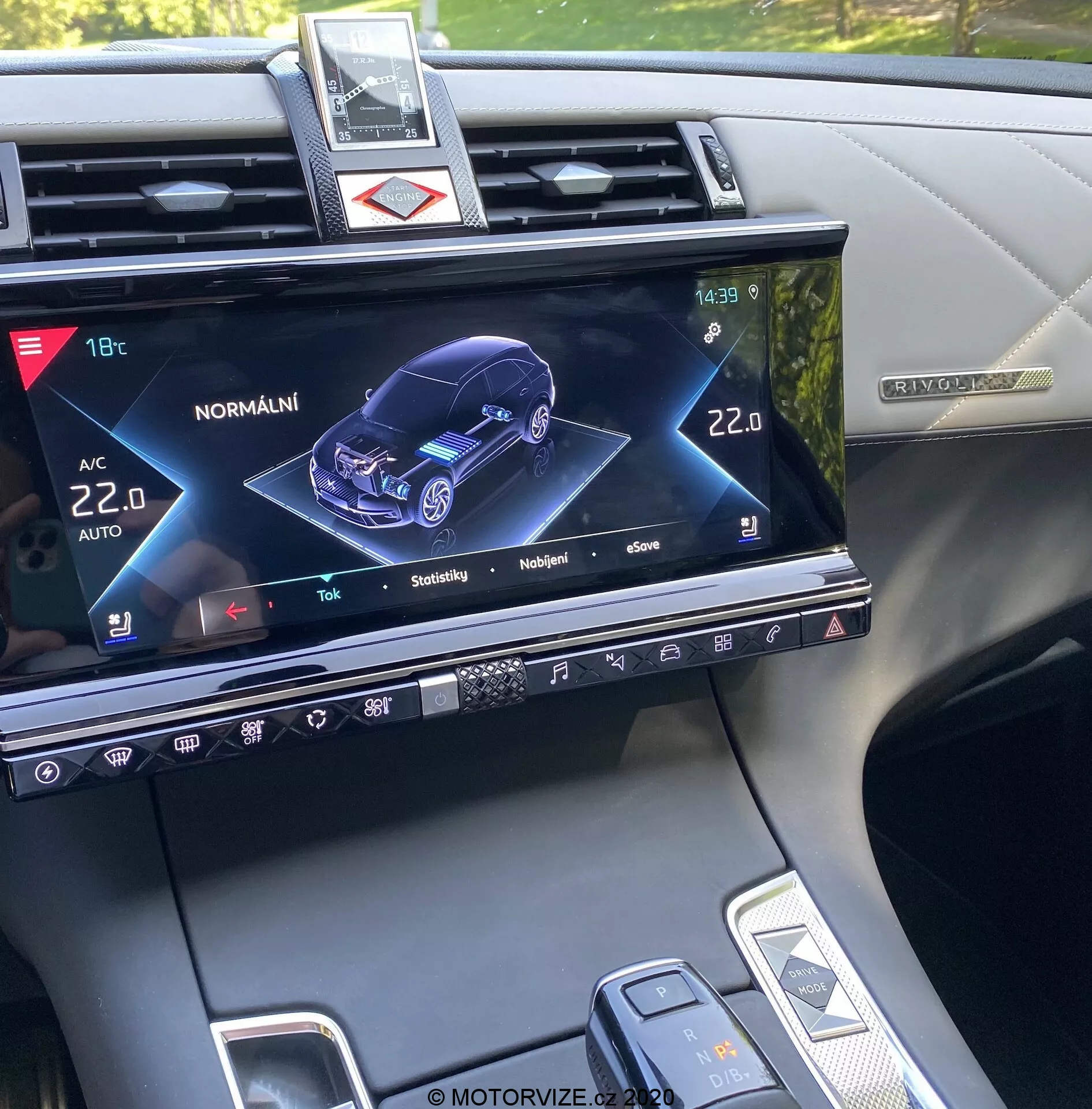 Sredinska konzola DS Automobiles DS-7 Crossback 2018, prikazuje zaslon sistemov za informiranje in razvedrilo z grafično 3D predstavitvijo avtomobila s prednjega desnega kota, kar nakazuje status in različne nastavitve, kot so nadzor klime, gretje sedežev in interaktivne funkcije modela avtomobila, skupaj s fizičnimi gumbi, občutljivimi na dotik, ter delnim prikazom prestavne ročice in izbirnika nastavitev vozila.