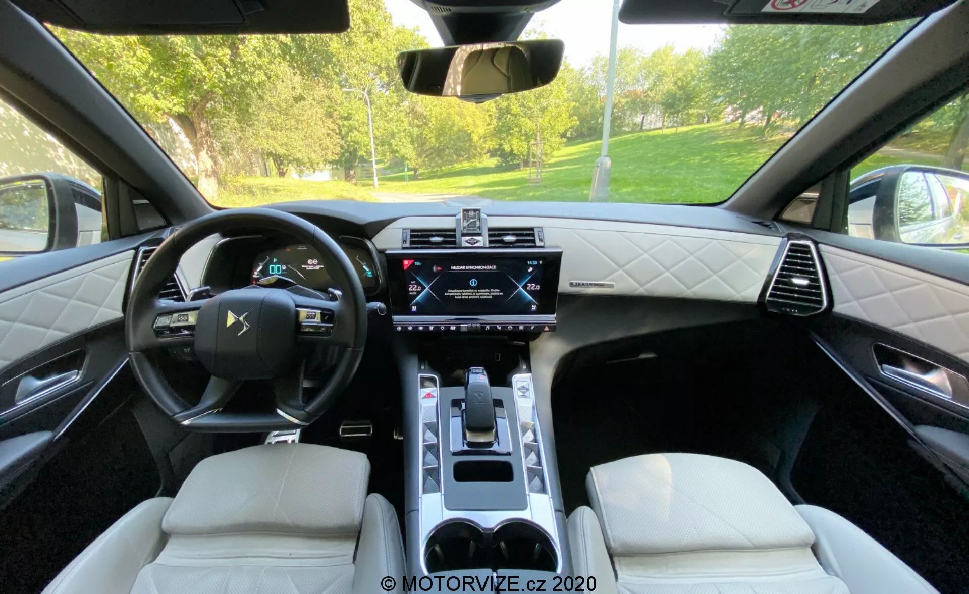 Posnetek notranjosti DS Automobiles DS 7 Crossback 2018 s pogledom iz zadnjih sedežev. Poudarjene so usnjeni večnamenski volan, digitalni instrumentni zaslon, osrednji zaslon na dotik za infotainment, nadzorna plošča za klimatske naprave, elektronski menjalnik, luksuzni usnjeni sedeži z diamantnim šivanjem ter sredinska konzola s držali za pijače. Slika prikazuje kombinacijo vrhunske tehnologije in prefinjenega oblikovanja.