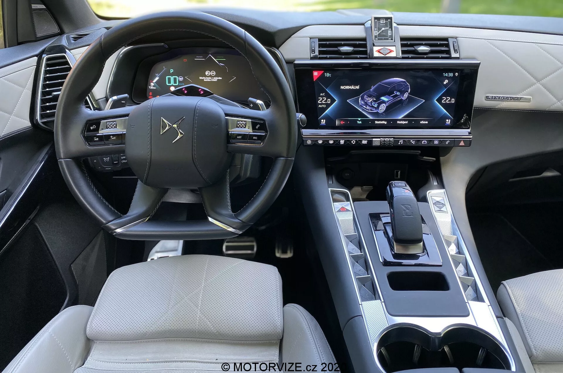 Notranjost DS Automobiles DS 7 Crossback 2018, pogled s zadnjega sedeža osredotočen na voznikovo stran. Lastnosti vključujejo volan z vgrajenimi kontrolami, digitalno instrumentno ploščo, centralno nameščen zaslon na dotik infotainment sistema, sodobno prestavno ročico, držala za pijačo in sofisticiran notranji dizajn z naprednimi tehnološkimi udobji.