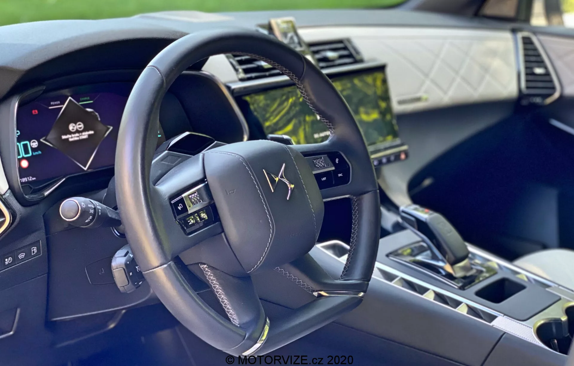 Notranji posnetek avtomobila DS-7 Crossback 2018 iz voznikove perspektive, ki prikazuje sodoben, večfunkcijski volan s kontrolnimi gumbi, digitalno instrumentno ploščo in zaslon na dotik infotainment sistema, ki poudarja napredno tehnologijo in luksuzne materiale.