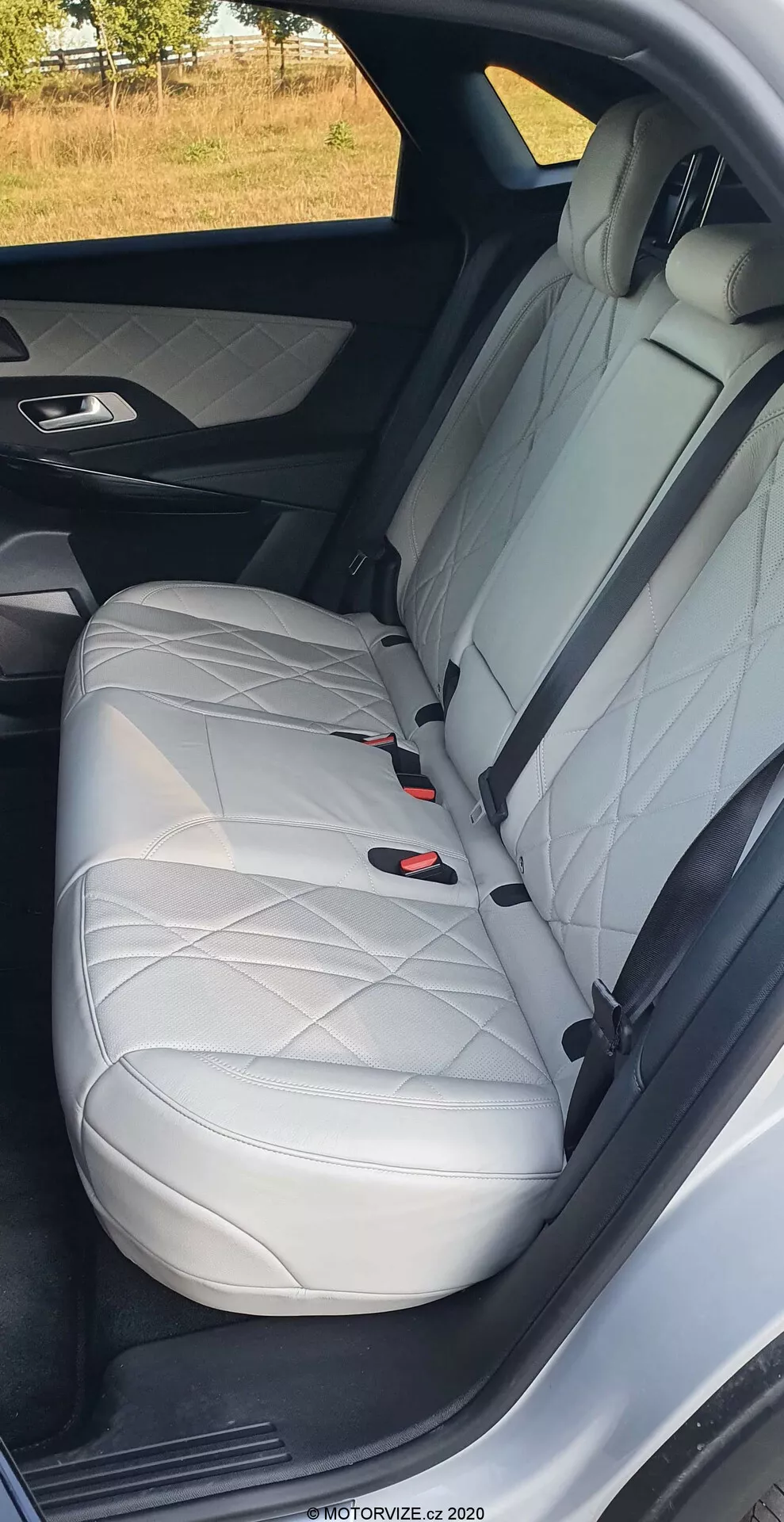 Bližnji pogled na zadnji sedež DS Automobiles DS-7 2018, ki prikazuje belo usnje z diamantnim šivom, vzglavnik, tritočkovni varnostni pas in sistem LATCH, poudarja luksuzno notranjo zasnovo in varnostne funkcije avtomobila