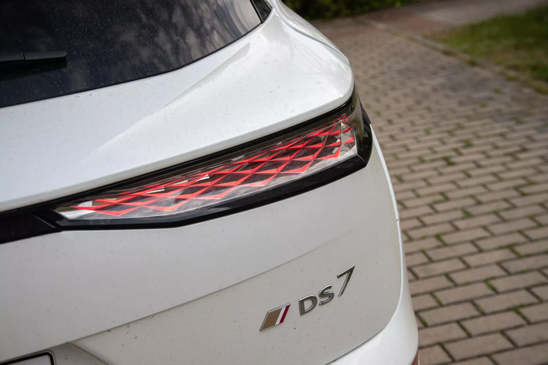 Posnetek zadnjega dela belega DS 7 z moderno LED zadnjo lučjo in emblemo modela, ki poudarja detajle oblikovanja in premijsko izvedbo