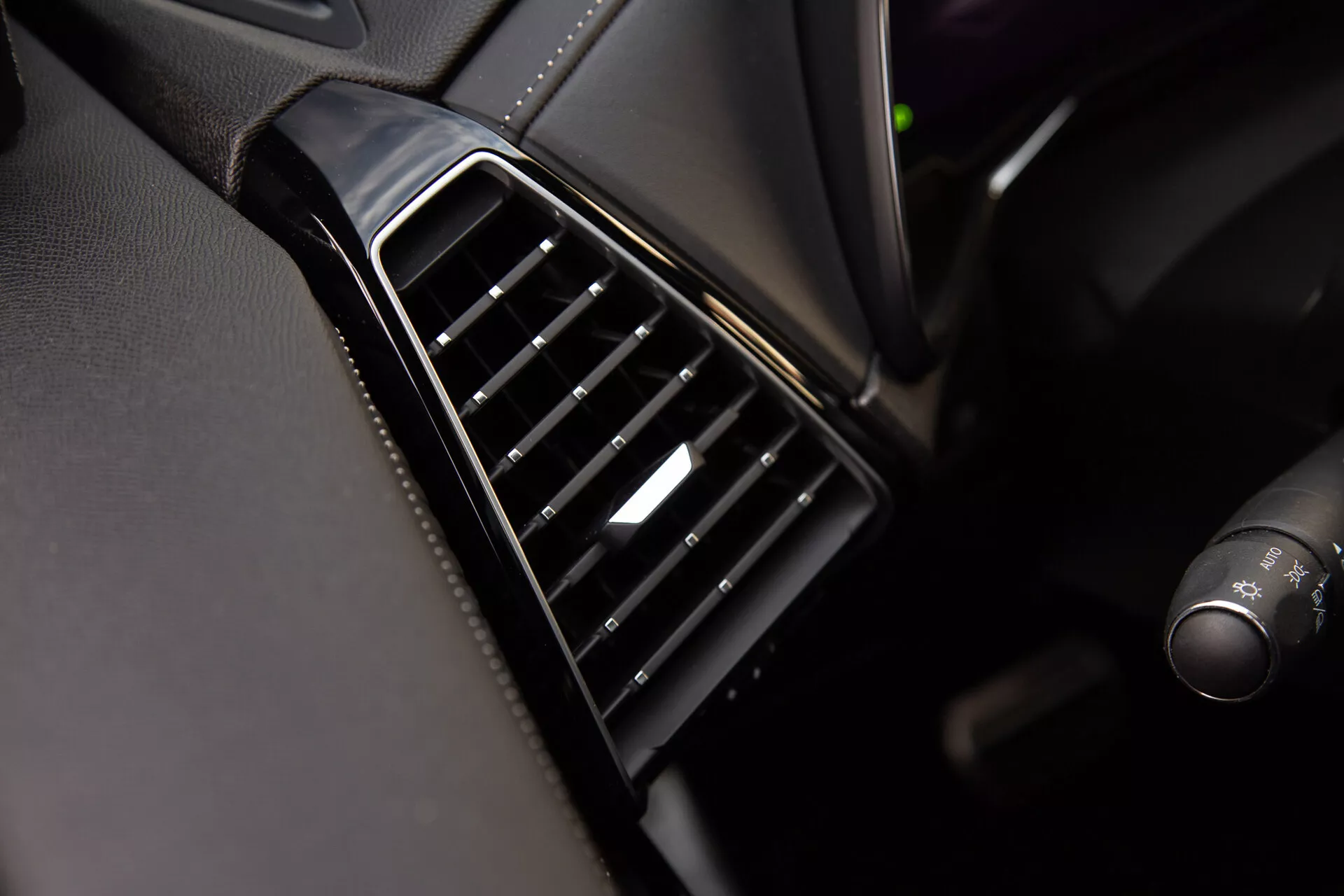 Podroben pogled na zračno režo DS Automobiles DS-7 2022 na armaturni plošči z navpično usklajenimi črnimi nastavljivimi lamelami, sijočim okvirjem in srebrnim poudarkom na krmilniku, ki prikazuje kakovost oblikovanja notranjosti in materialov vozila