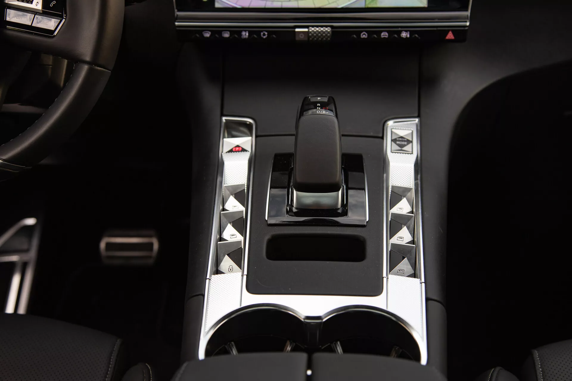 Podroben pogled na sredinsko konzolo DS Automobiles DS-7 2022 z ergonomsko prestavno ročico, kovinskimi poudarki, edinstvenimi nadzornimi gumbi, zaslonom na dotik in dvojnimi držali za kozarce, ki poudarjajo napredne elemente nadzora vozila in elemente razkošnega oblikovanja.