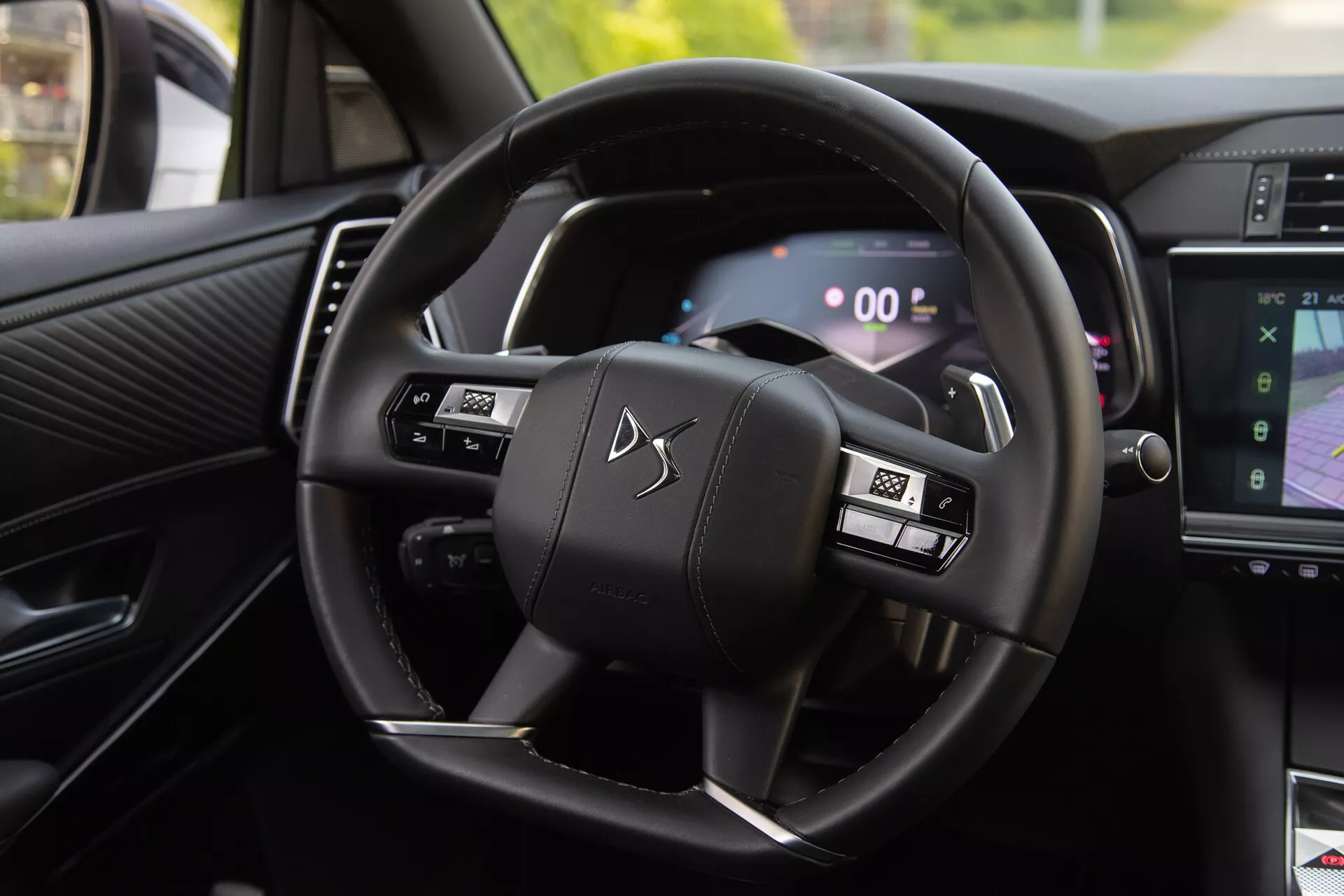 Notranji pogled na DS Automobiles DS-7 2022, ki prikazuje volan z večfunkcijskimi gumbi in digitalno instrumentno ploščo, vključno s prestavnimi ročicami in delom sistema za informacije in zabavo, ki prikazuje navigacijo
