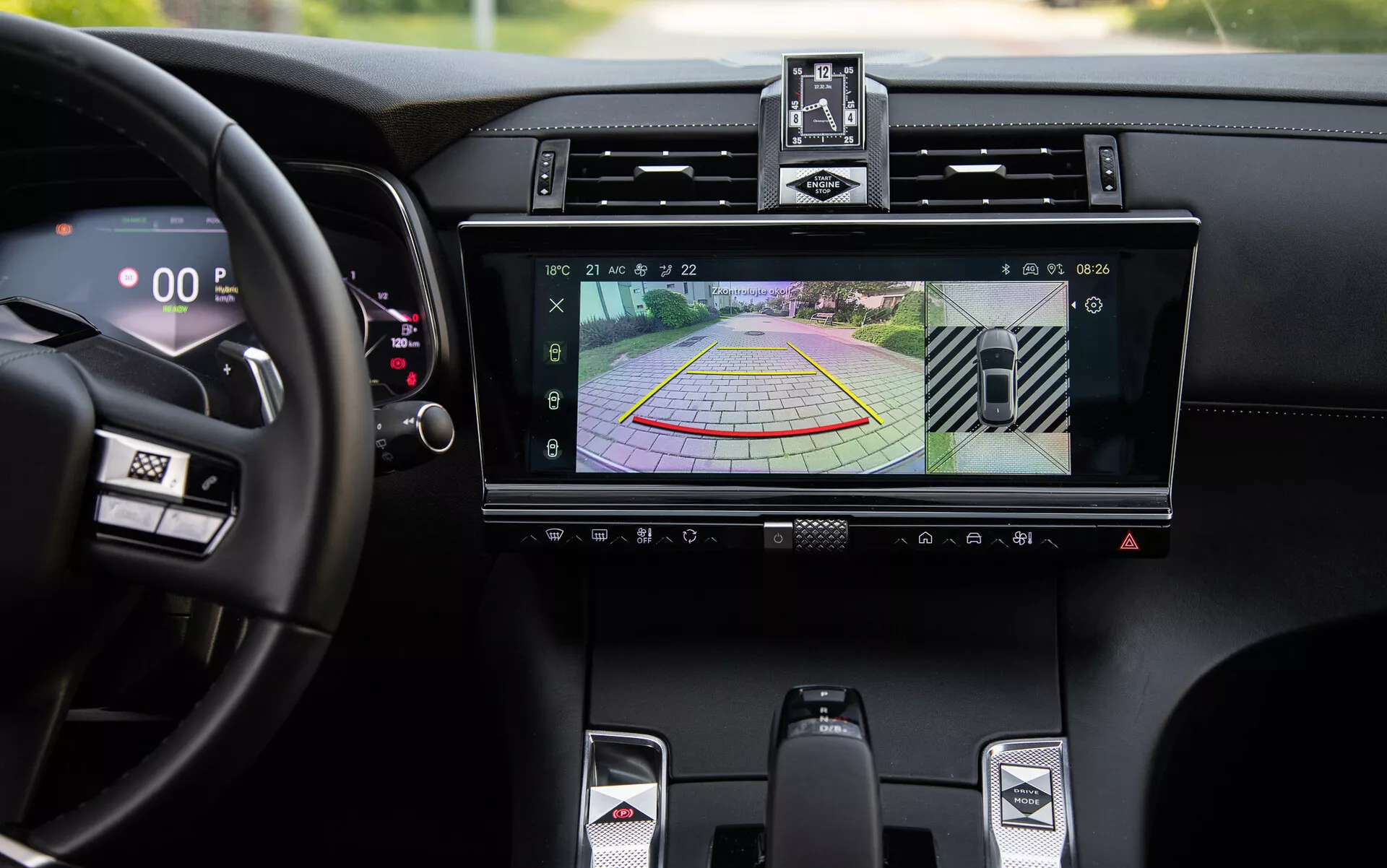 Podrobnost razkošne notranjosti DS-7 2022 z infotainment sistemom, ki prikazuje zaslon kamere za vzvratno vožnjo in dinamične smernice za asistenco pri parkiranju, centralne zračnike, gumbe za klimatsko napravo, športno prestavno ročico in digitalni hitrostomer