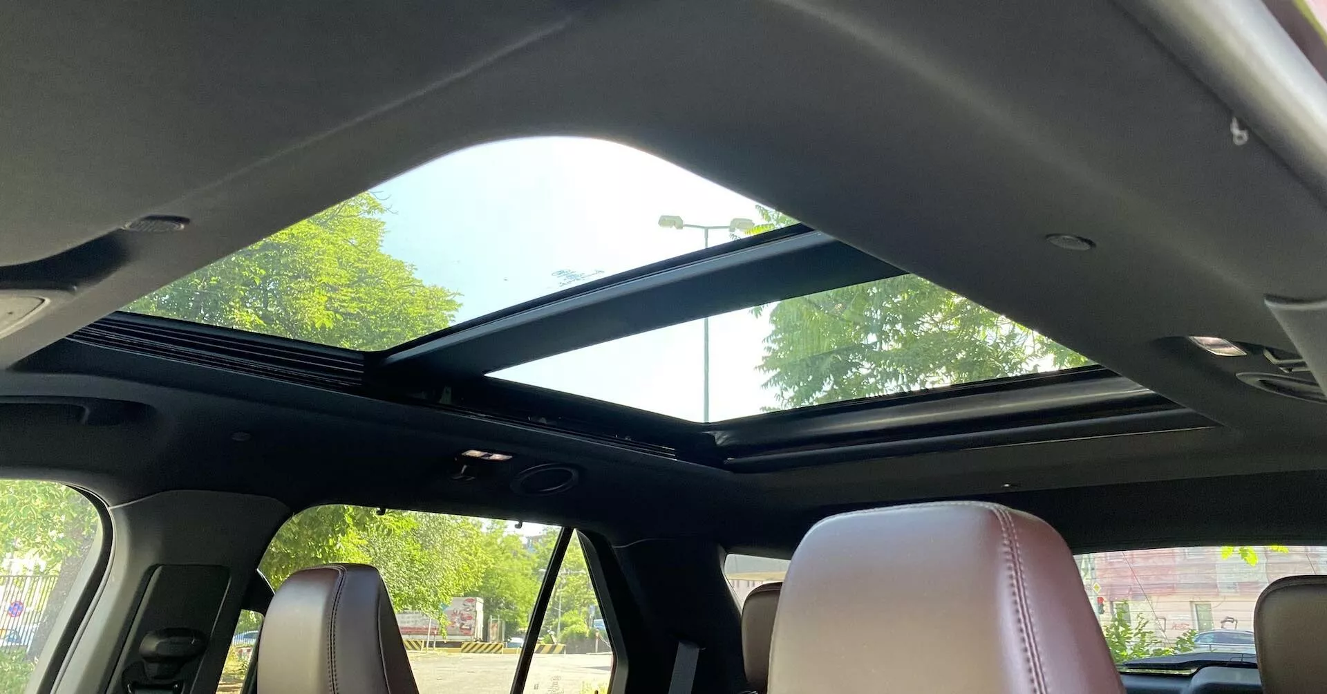Notranji pogled na Ford Explorer 2019 s poudarkom na panoramski strehi iz zadnjega sedeža. Streha se razteza od spredaj proti zadnji strani z velikim steklenim panelom, ki omogoča veliko naravne svetlobe, dopolnjeno z odprto zložljivo senčnico. Sprednji del strehe vsebuje nadzorne elemente na zgornji konzoli in bralno lučko. Temna stropna obloga kontrastira s svetlejšimi usnjenimi sedeži, prikazovanje sodobnega oblikovanja in luksuznih notranjih lastnosti.