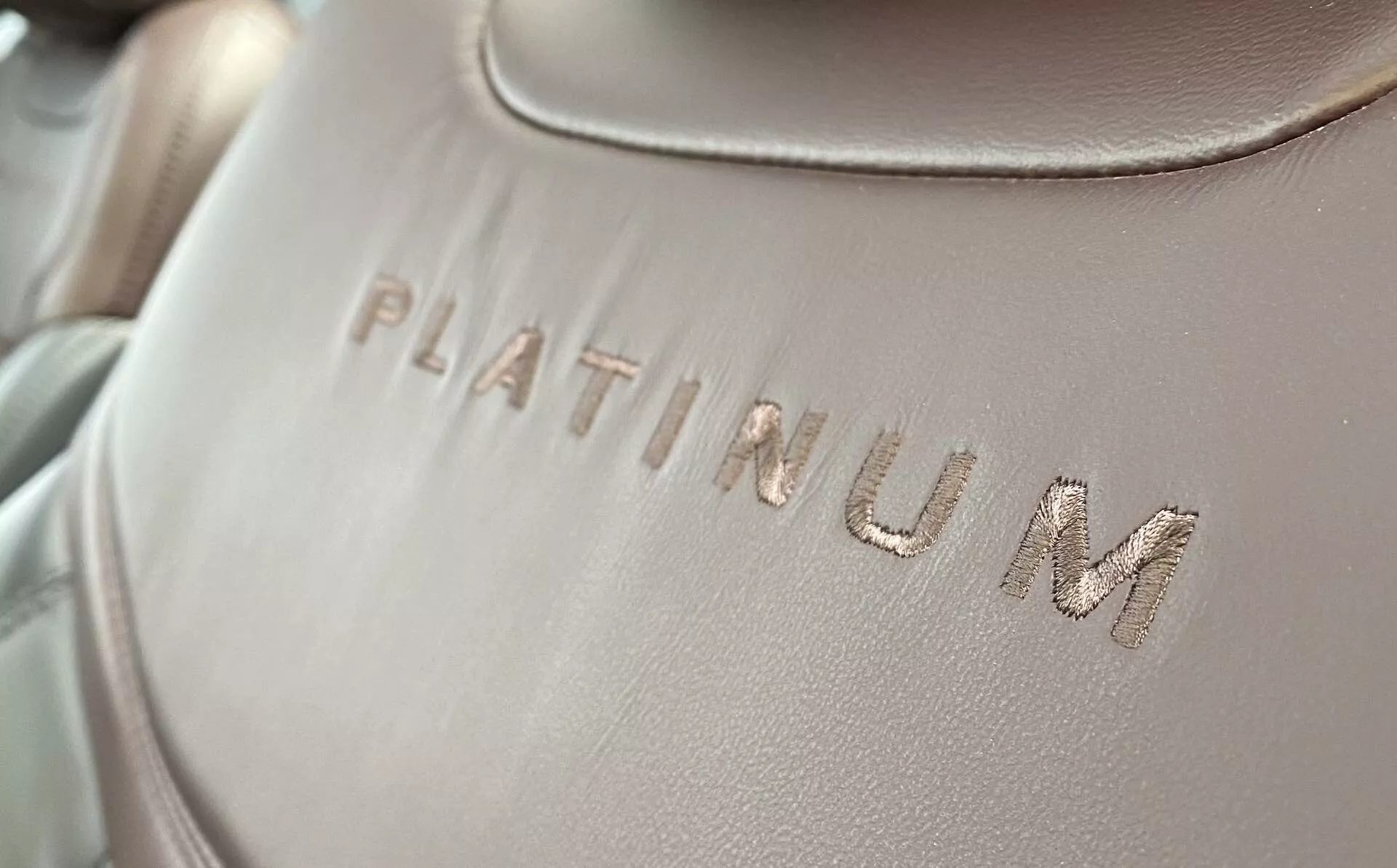 Podroben posnetek notranje oblazinjenja Forda Explorer 2019, kjer je beseda 'PLATINUM' vtisnjena na gladko tkanino ali usnjeno površino, z rahlim diagonalnim kotom. Besedilo je v fokusu, z mehko, enakomerno porazdeljeno osvetlitvijo in plitko globinsko ostrino.