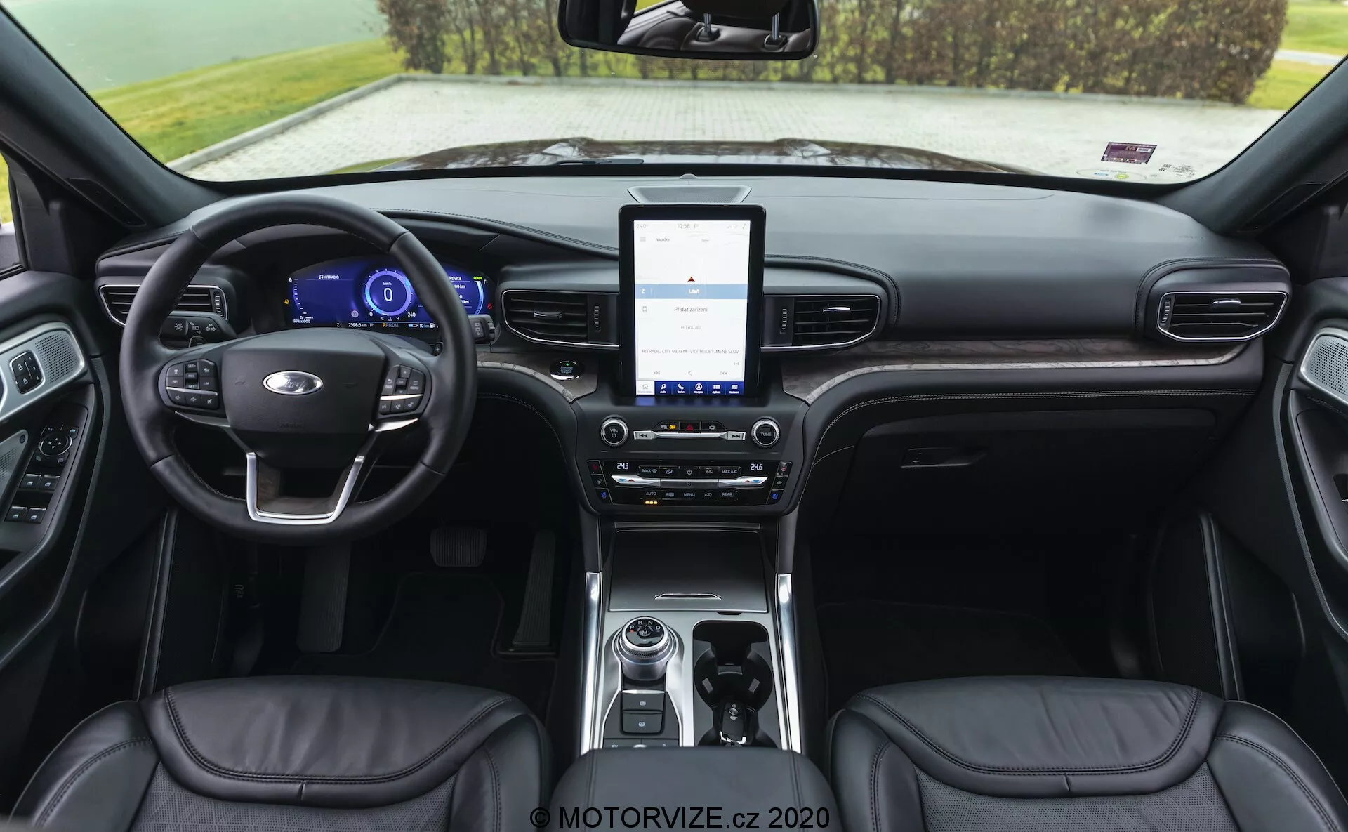 Notranjost kabine Ford Explorerja iz leta 2019 prikazuje armaturno ploščo iz pogleda proti zadnjemu delu. Pogled vključuje usnjen volan z vgrajenimi kontrolami, digitalno instrumentno ploščo, velik zaslon na dotik infotainment sistema, dvopodročno klimatsko kontrolo, rotacijsko prestavno ročico, shranjevalni prostor z možnostmi povezljivosti, usnjene sedeže z vidnimi šivi in delno vidne vratne plošče s kontrolami.