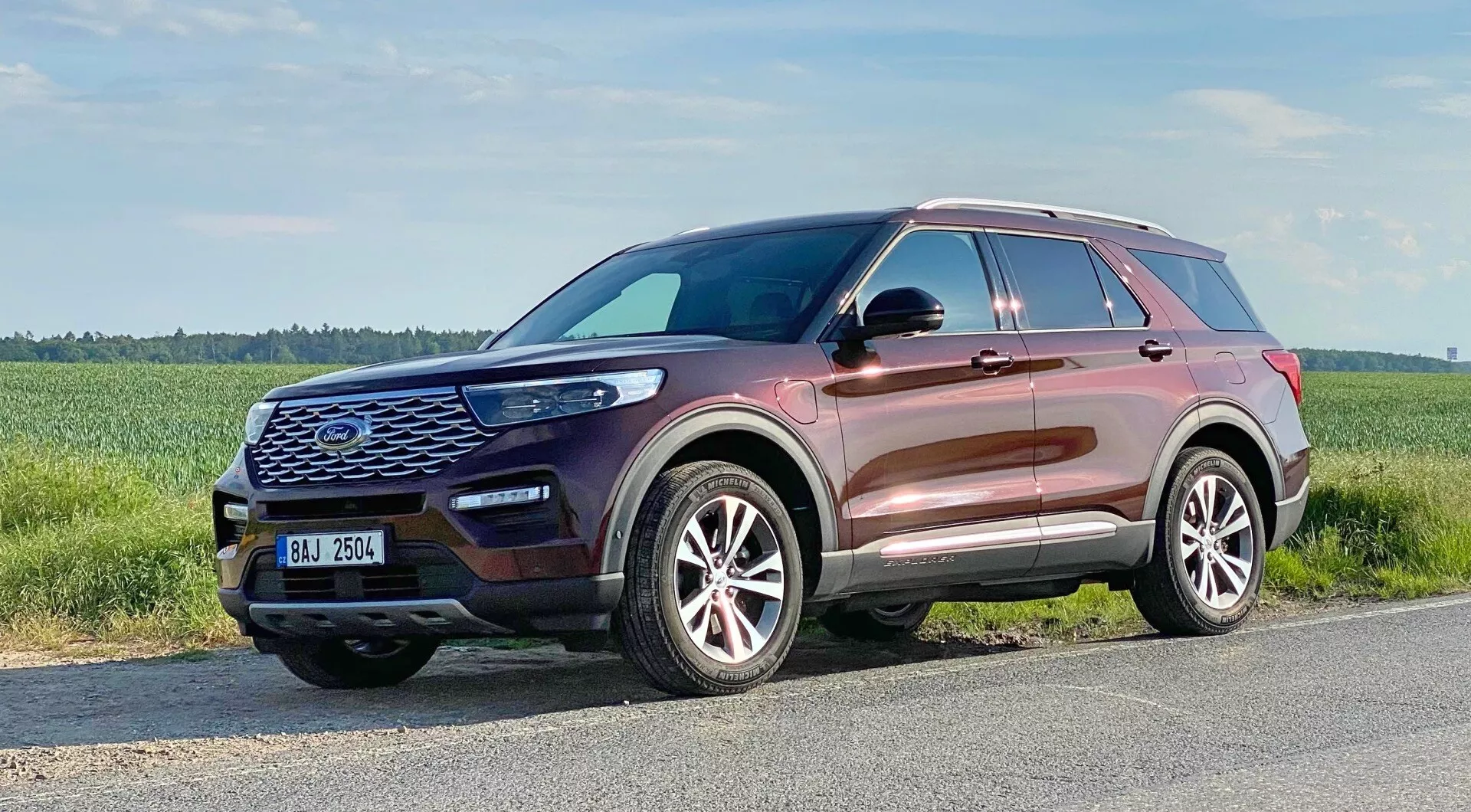 Ford Explorer 2019 - Sodobni SUV, zajet iz tričetrtinskega sprednjega pogleda, ki poudarja sprednjo masko s šesterokotnim vzorcem in velikim emblemom, konturirano pokrovom motorja, elegantnimi LED žarometi, meglenkami, vstopnimi ventilacijskimi odprtinami, večkrakimi aluminijastimi platišči, rahlo naraščajočo linijo oken, strešne nosilce, bočne ogledala z vgrajenimi smerniki in kovinsko barvo karoserije, ki odraža visokokakovostno končno obdelavo.