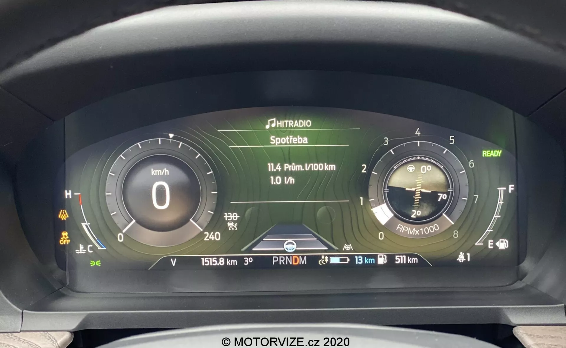 Pogled od blizu na napredno digitalno instrumentno ploščo Ford Explorerja 2019 iz voznikove perspektive, s hitrostnim merilnikom v kilometrih na uro, simuliranim analognim merilnikom vrtljajev, večnamenskim prikazovalnikom z medijskimi in potovalnimi podatki, odčitkom merilnika prevoženih kilometrov 15158 km, indikatorjem temperature hladnega motorja, skoraj polnim merilnikom goriva in več opozorilnimi lučkami.