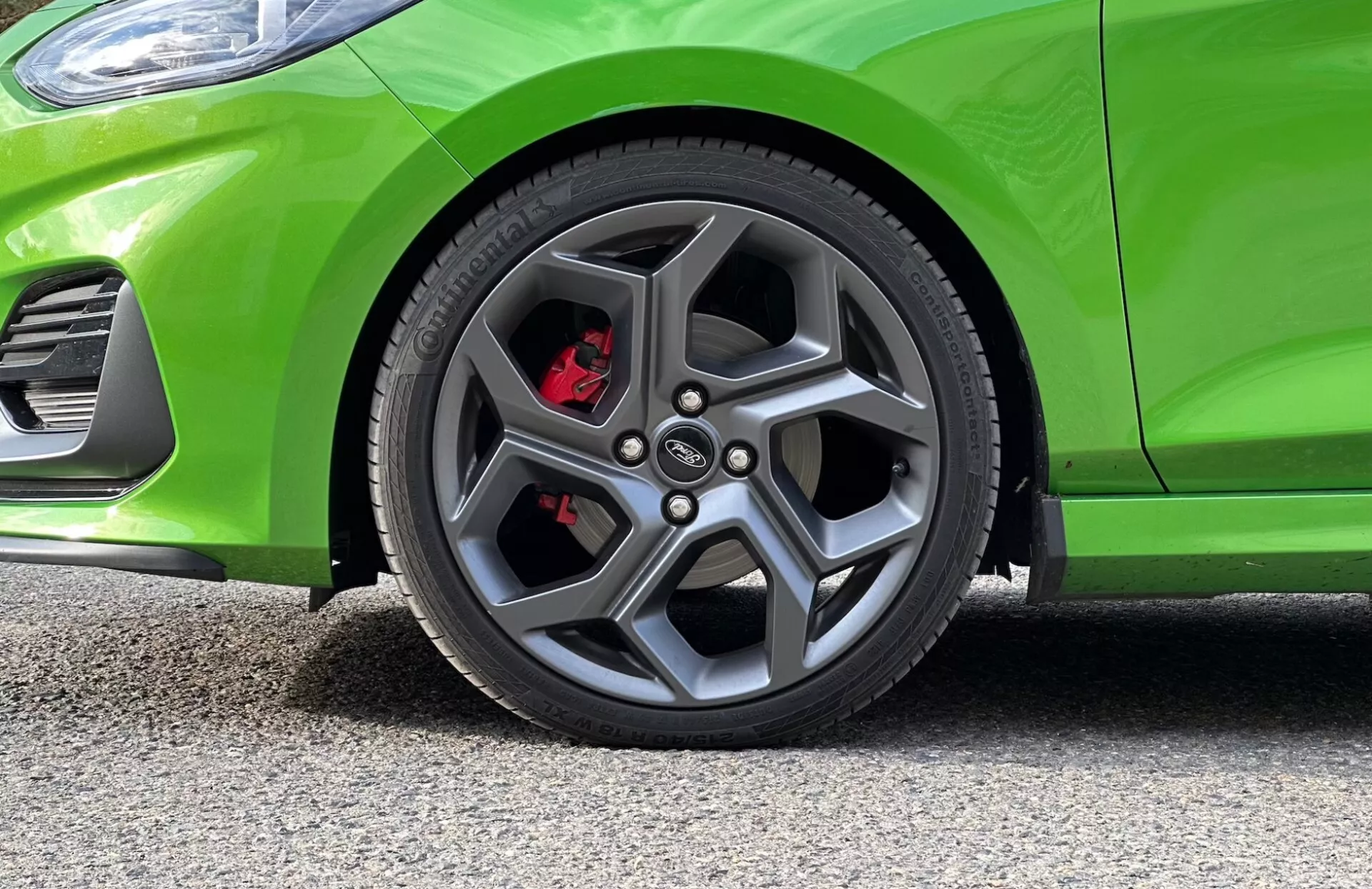 Podroben pogled na sprednje kolo in delni pogled na sprednjo stran Ford Fiesta 2022, ki prikazuje sodobno zasnovo zlitinskega kolesa, zmogljive rdeče zavorne čeljusti in živo zeleno barvo